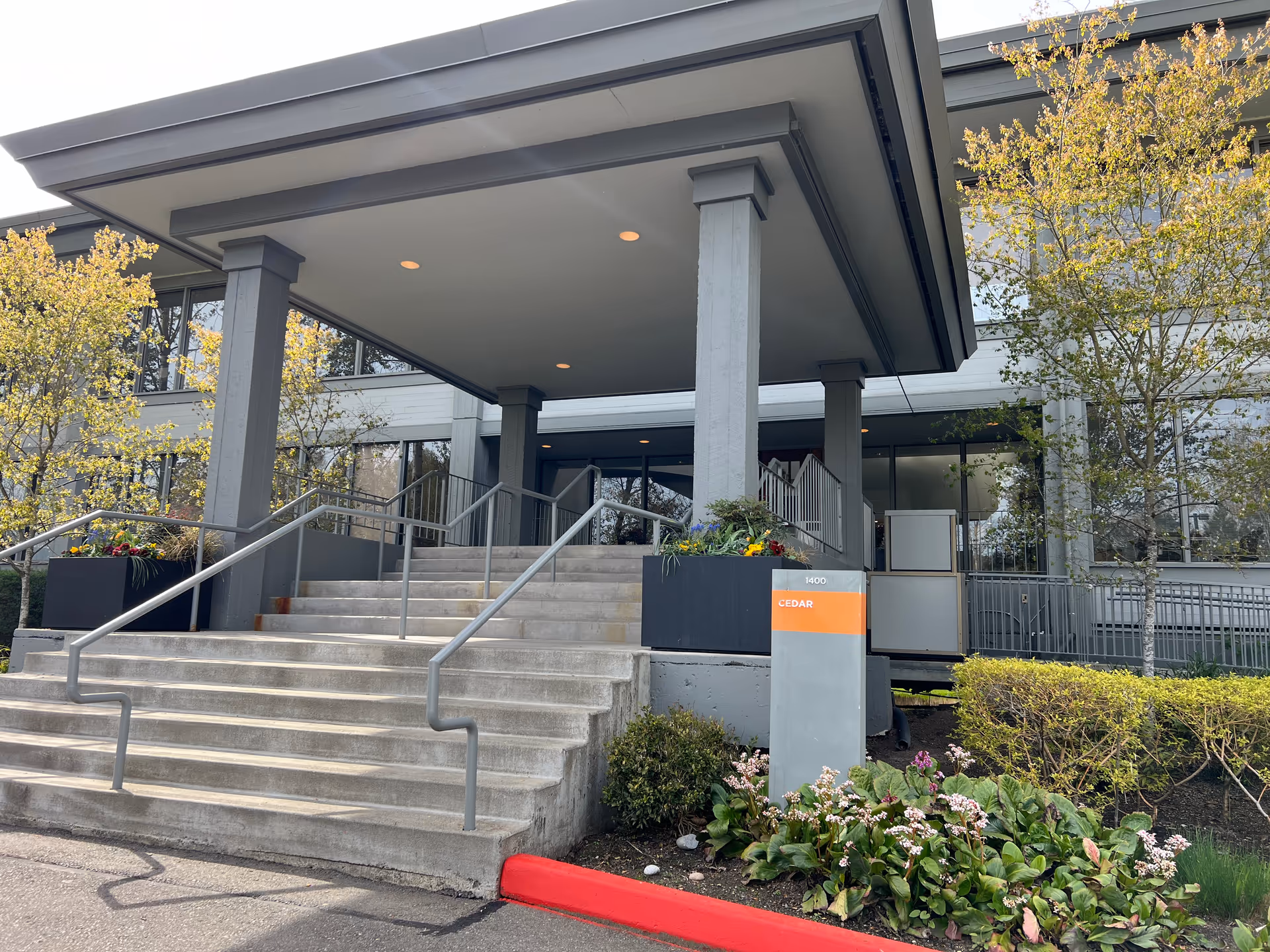 Modern senior living facility entrance with stairs, a covered porte-cochere, and landscaping.
