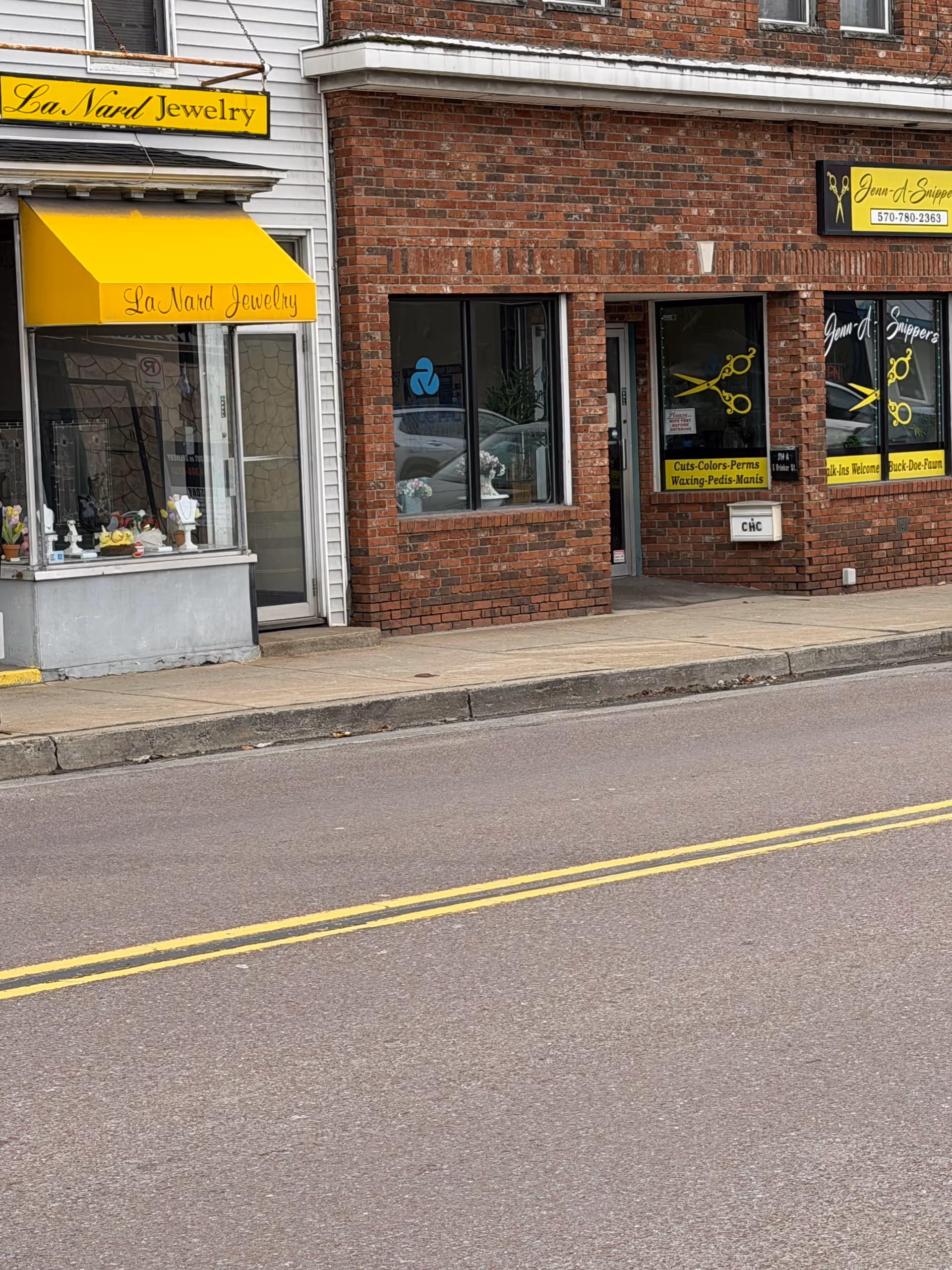 Brick storefronts line a sidewalk, including a jewelry shop with yellow awning on left.
