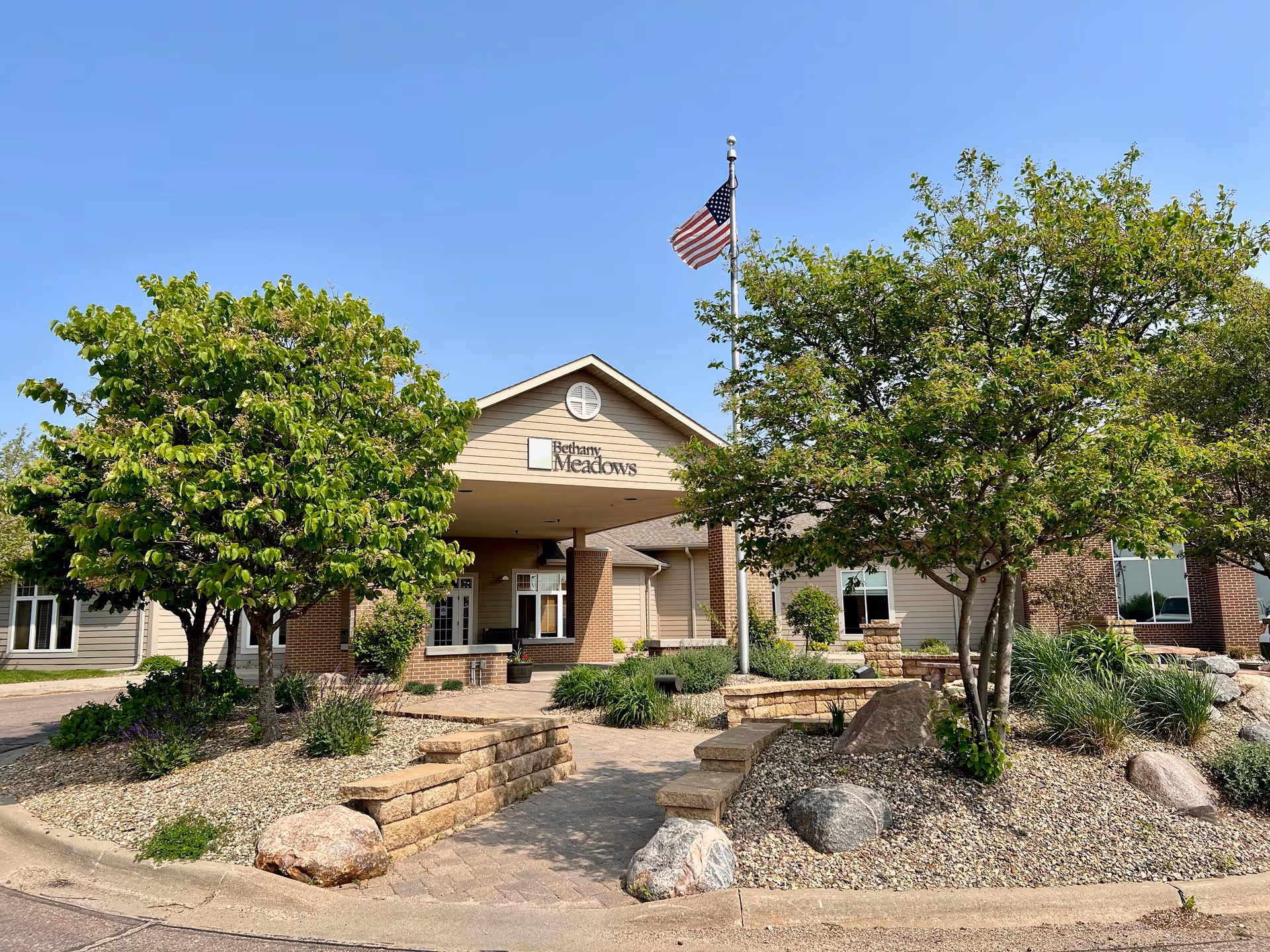 Exterior view of Bethany Meadows facility with trees, landscaping, and a flag near the entrance.