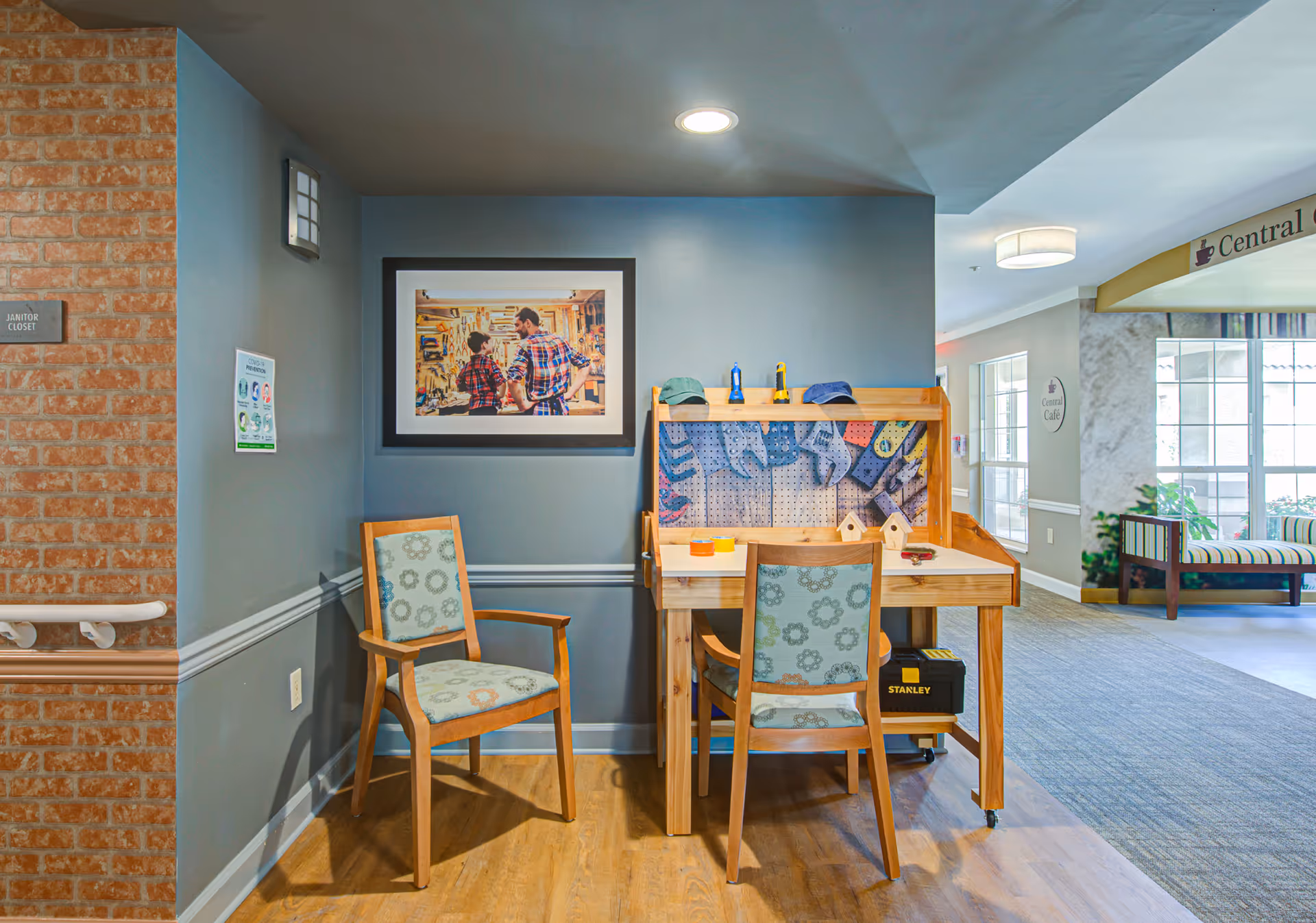 Indoor activity desk with pegboard, chairs, and framed art in a senior living facility.