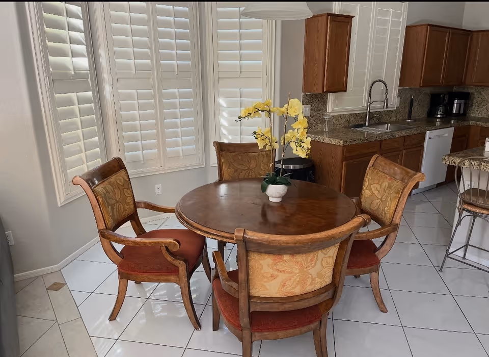Round wooden dining table with four upholstered chairs in a kitchen and dining area, orchid centerpiece.