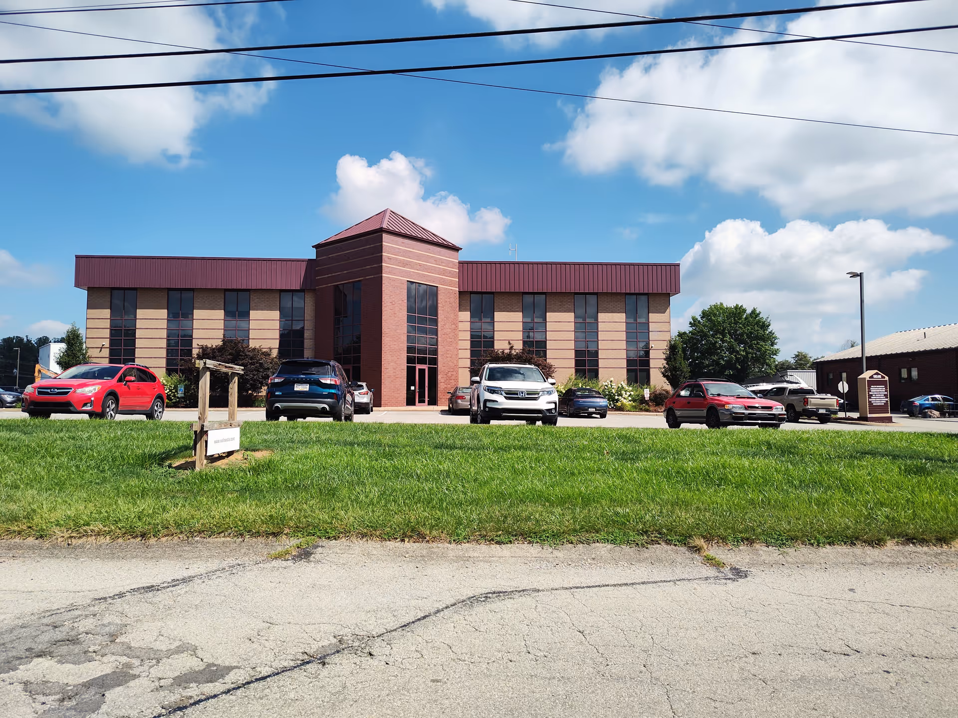 Exterior view of a brick hospice facility with a parking lot and blue sky.