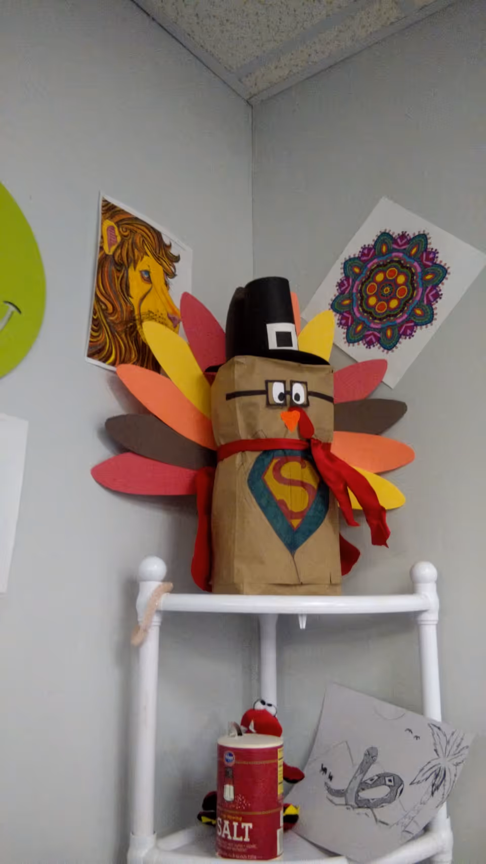 Colorful turkey-shaped craft with a pilgrim hat sits on a white shelf in a decorated room.