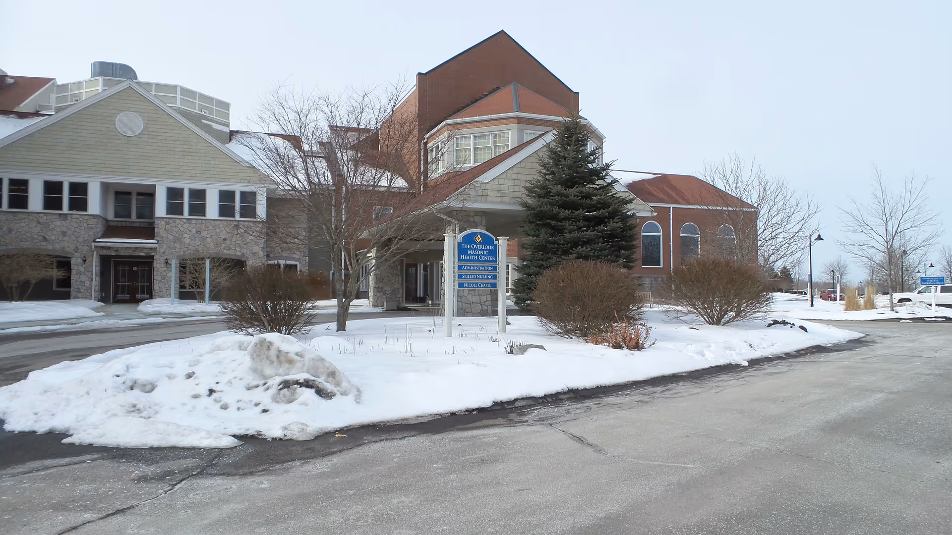 Winter exterior of a brick and stone building labeled Overlook Hospice Services, snow-covered driveway.