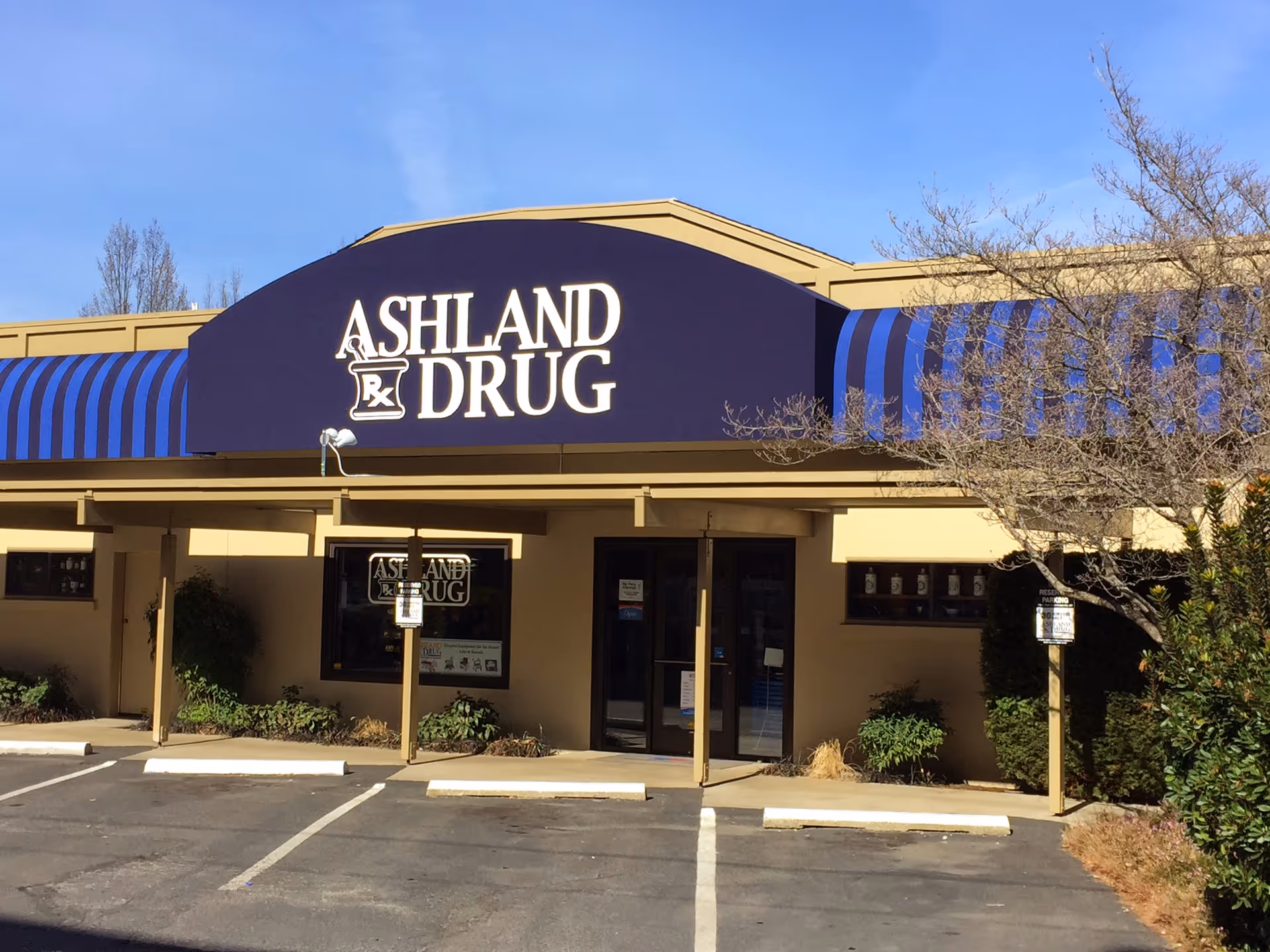 Front view of an Ashland Drug storefront with purple signage and striped awning.