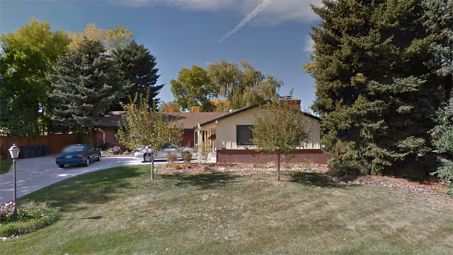 Single-story senior home with driveway, parked car, and well-kept lawn surrounded by trees.