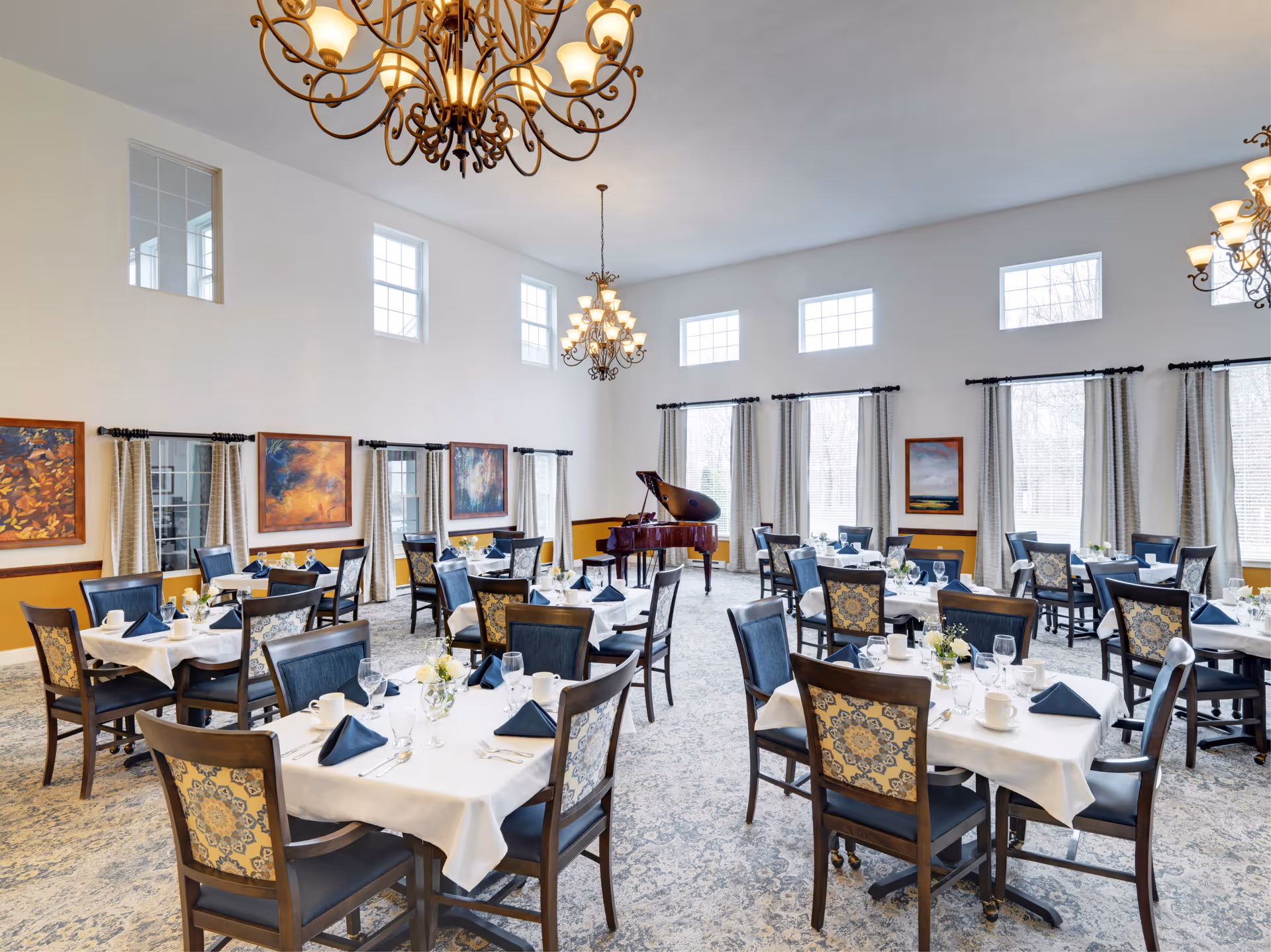 Elegant dining room with neatly set tables, chandeliers, and a grand piano.