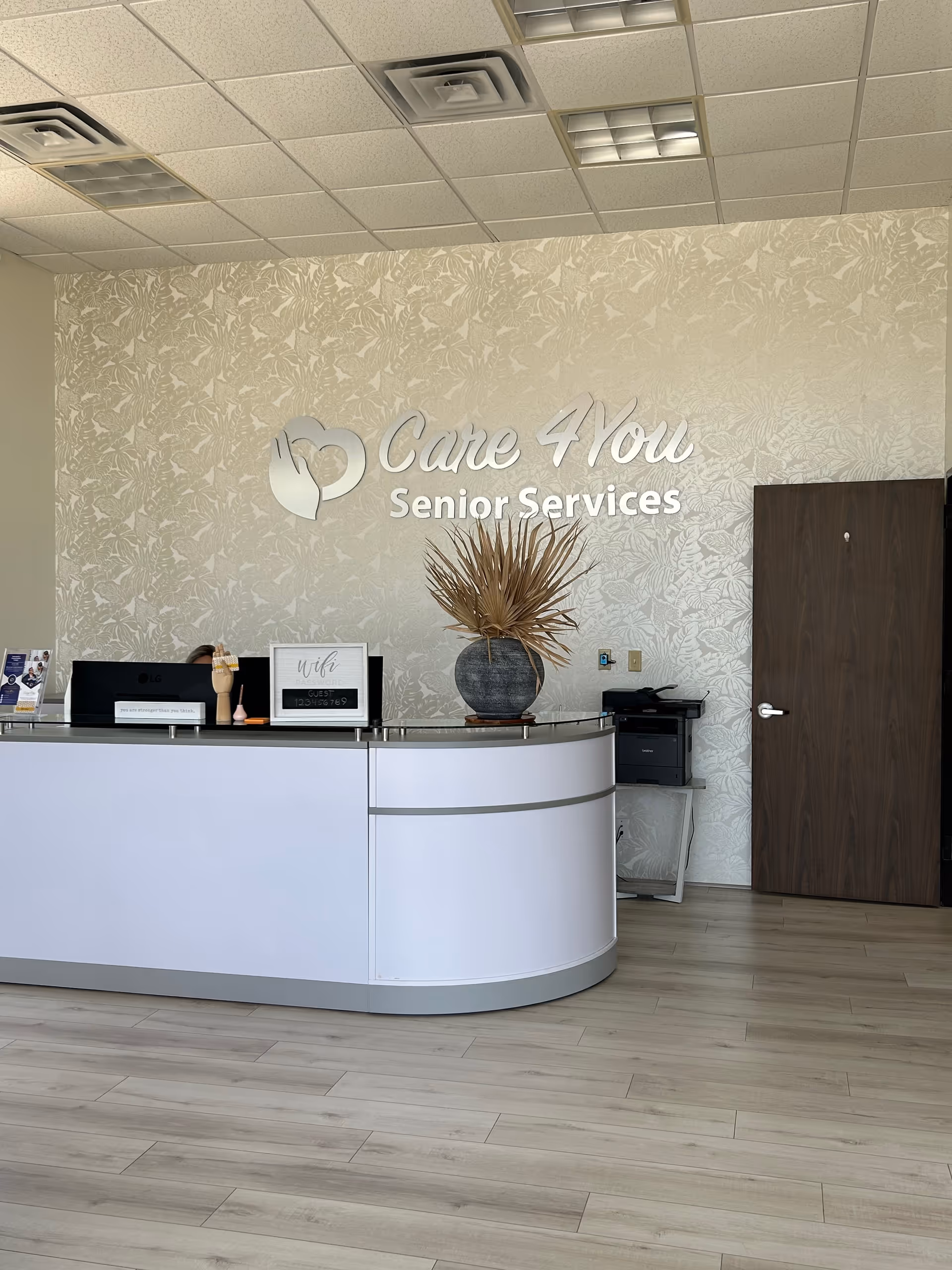 A modern reception desk in Care 4 You Senior Services with patterned wallpaper and plant.