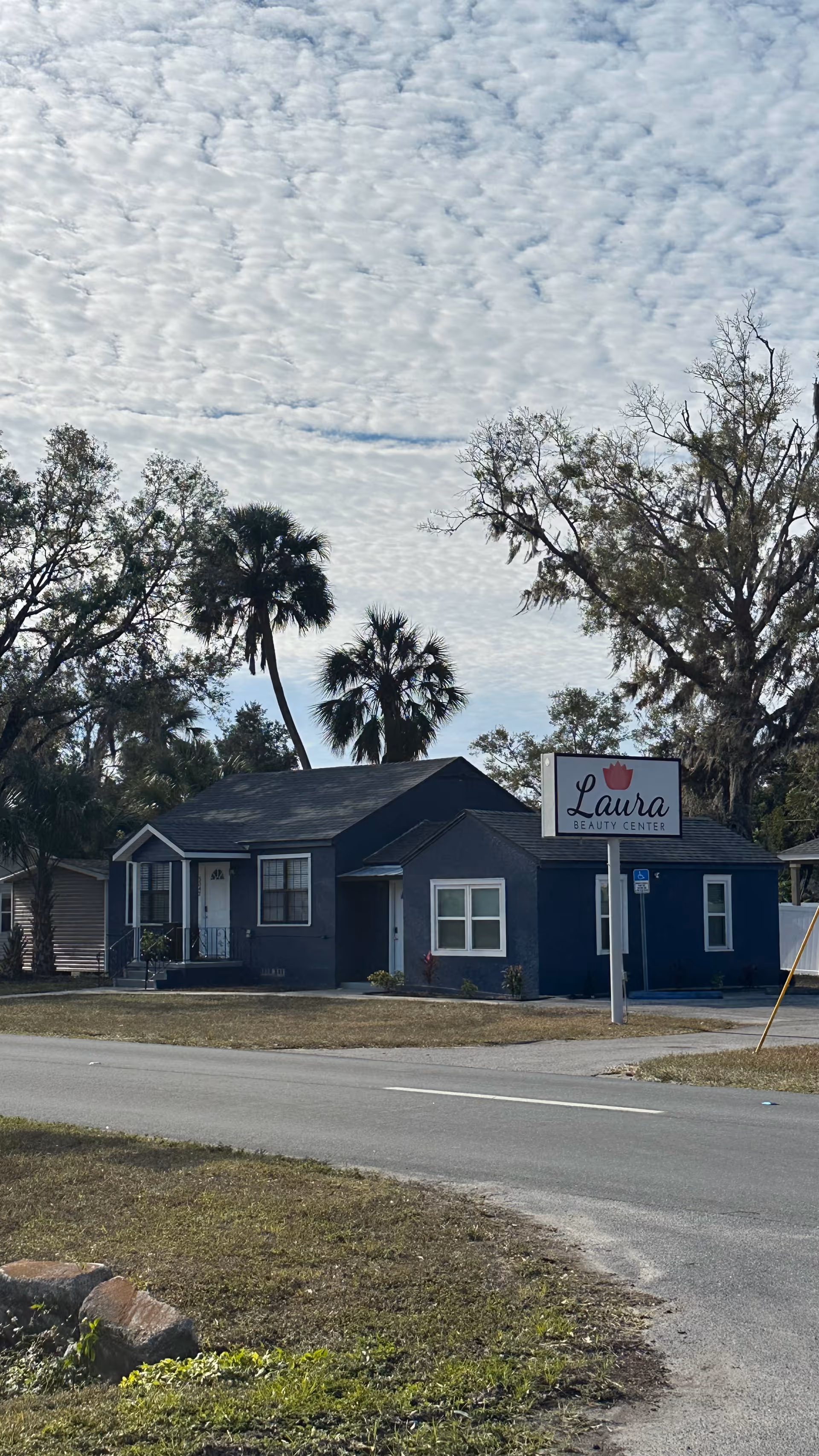 Blue single-story building with a Laura Beauty Center sign beside a road, palm trees nearby.