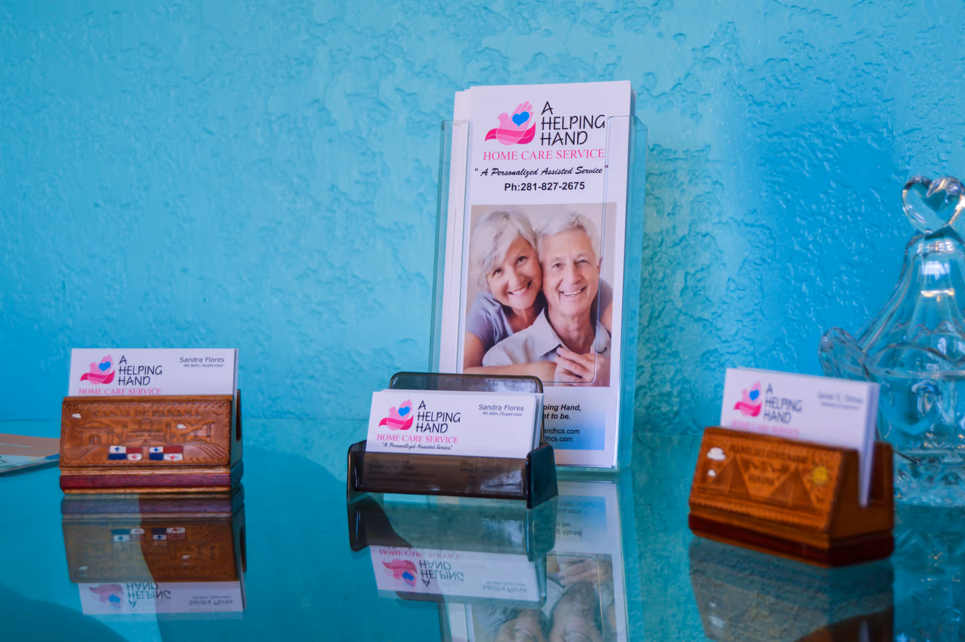 Brochure stand and card holders on a glass counter against a turquoise wall.