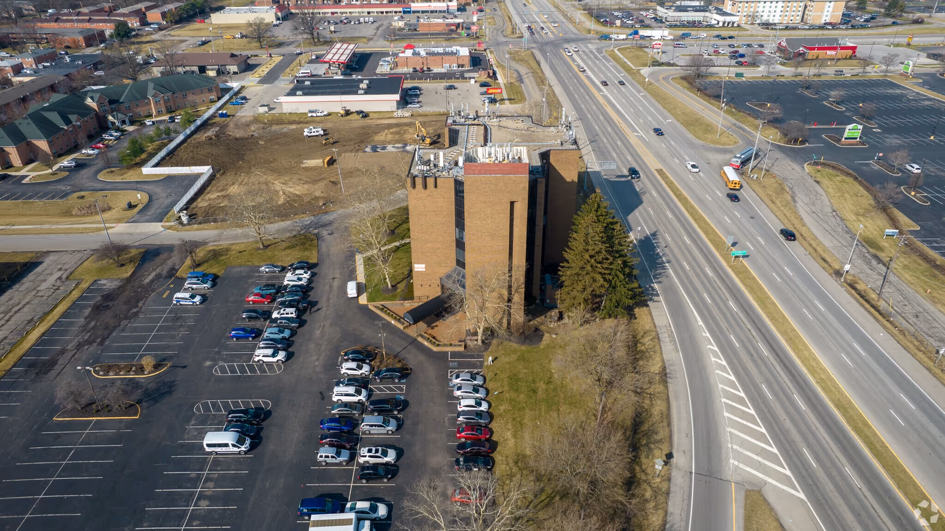 Aerial view of a brick multi-story building with parking lot and surrounding roads.