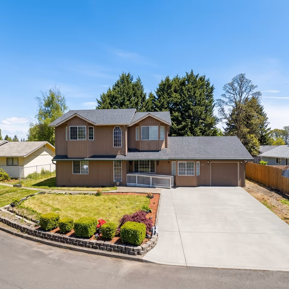 Two-story brown house with a manicured lawn and attached garage in a suburban neighborhood.
