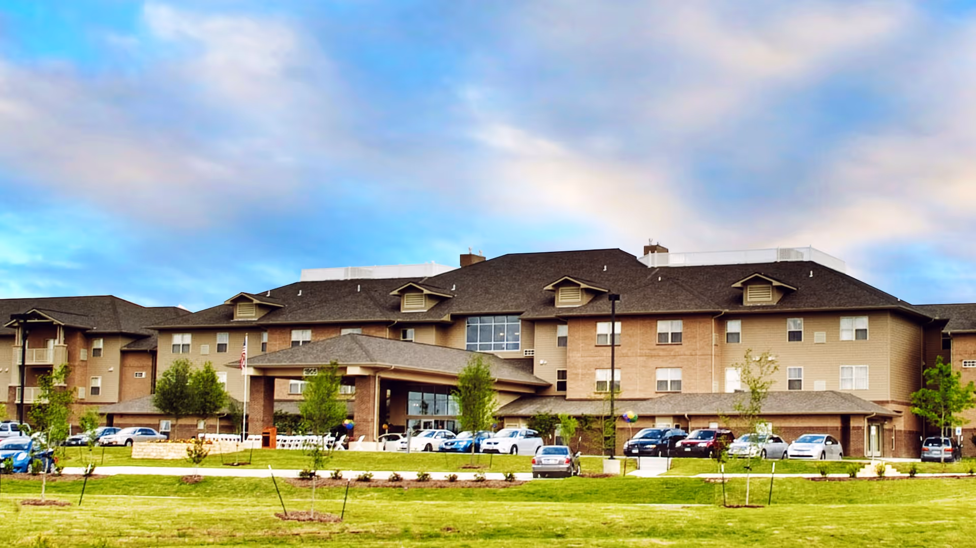 Multi-story senior living facility with brick facade, entrance canopy, and surrounding manicured lawn.