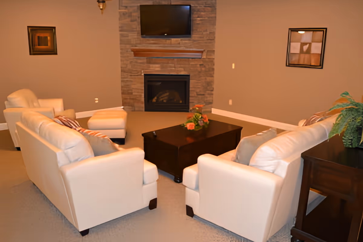 Cozy living room with two cream sofas facing a dark coffee table and a stone fireplace with a TV mounted above.