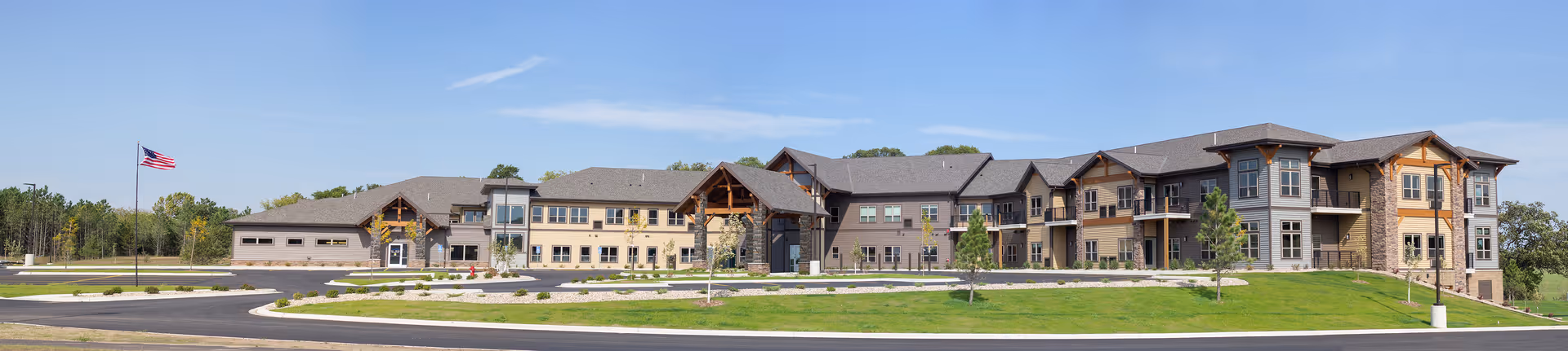 A long, multi-section senior living facility exterior with stone accents and an American flag.