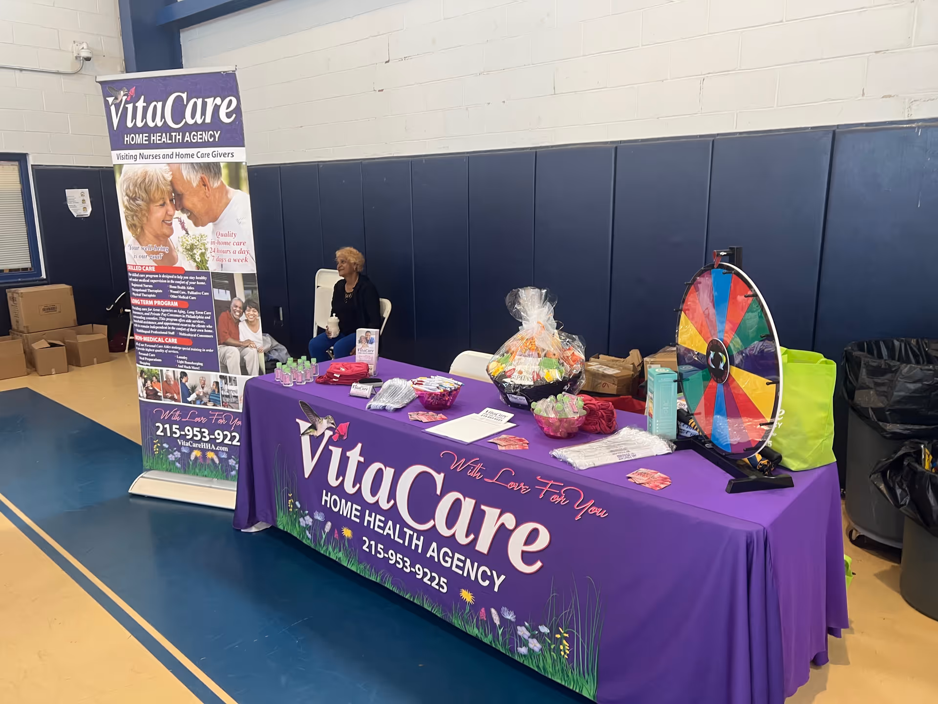 Indoor event booth for VitaCare Home Health Agency with purple table display and prize wheel.