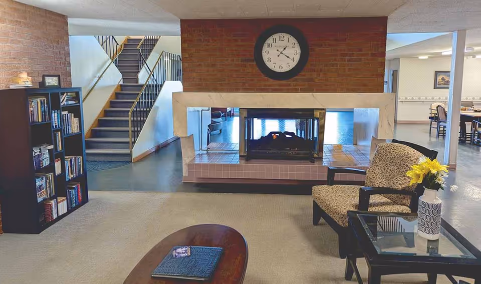 Senior living facility lobby featuring a brick fireplace, clock, bookshelves, and seating.
