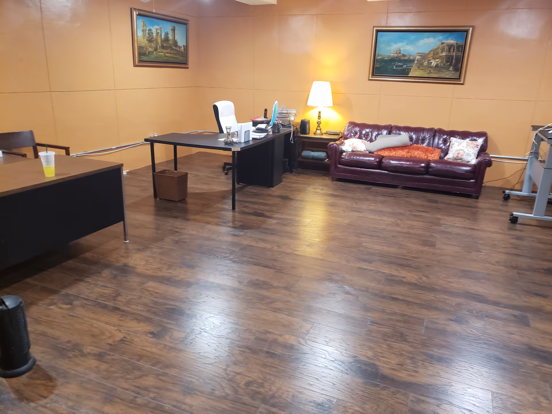 A spacious lounge with a desk, leather sofa, lamp, and framed wall art.