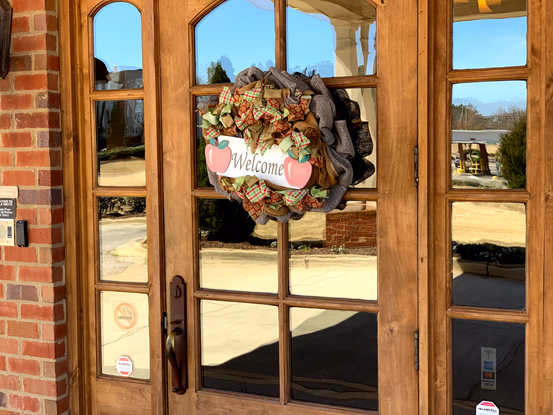 Wooden glass doors with a wreath and 'Welcome' sign at a brick entrance.