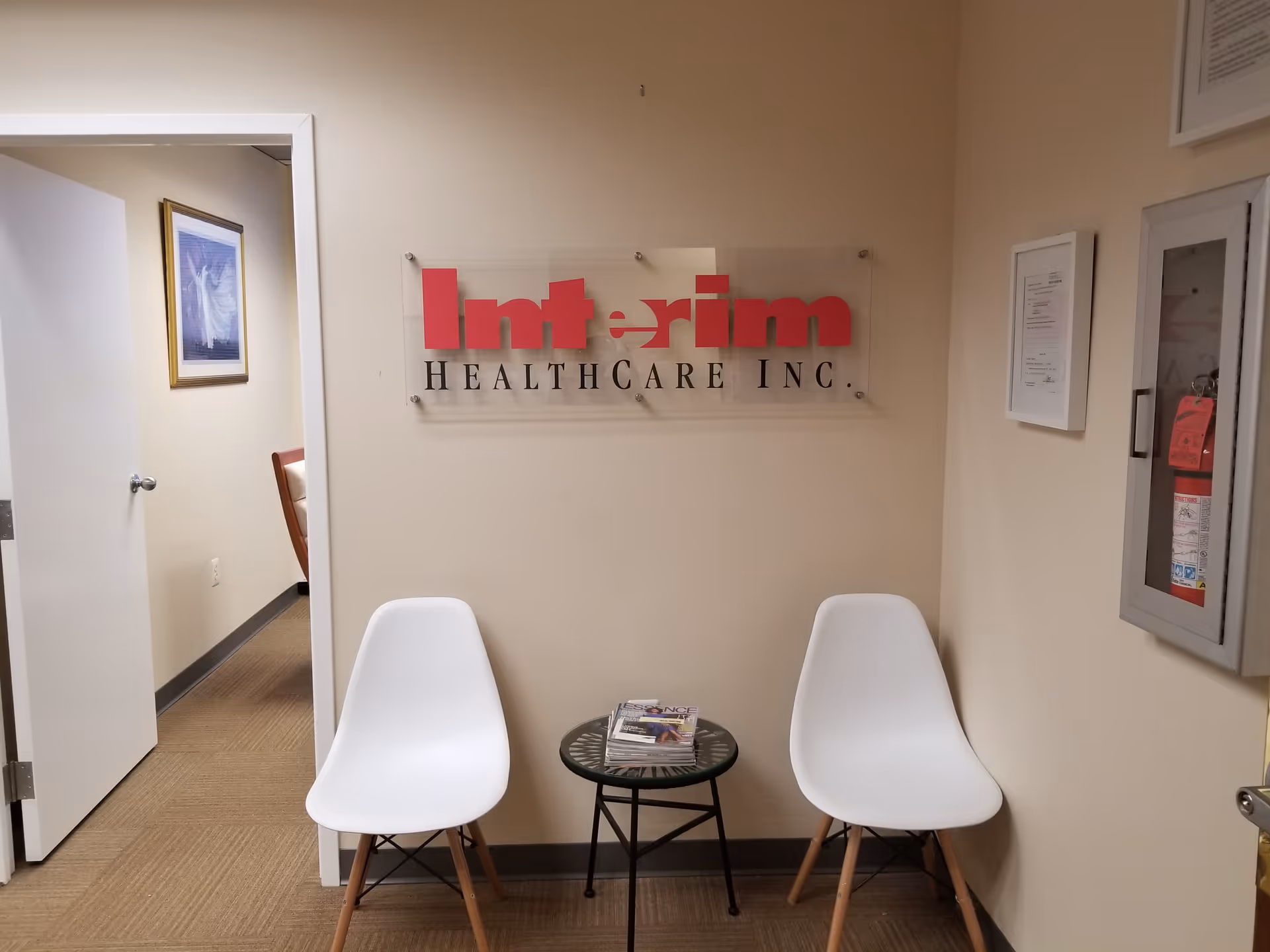 Lobby seating area with two white chairs and a small table under Interim HealthCare sign.