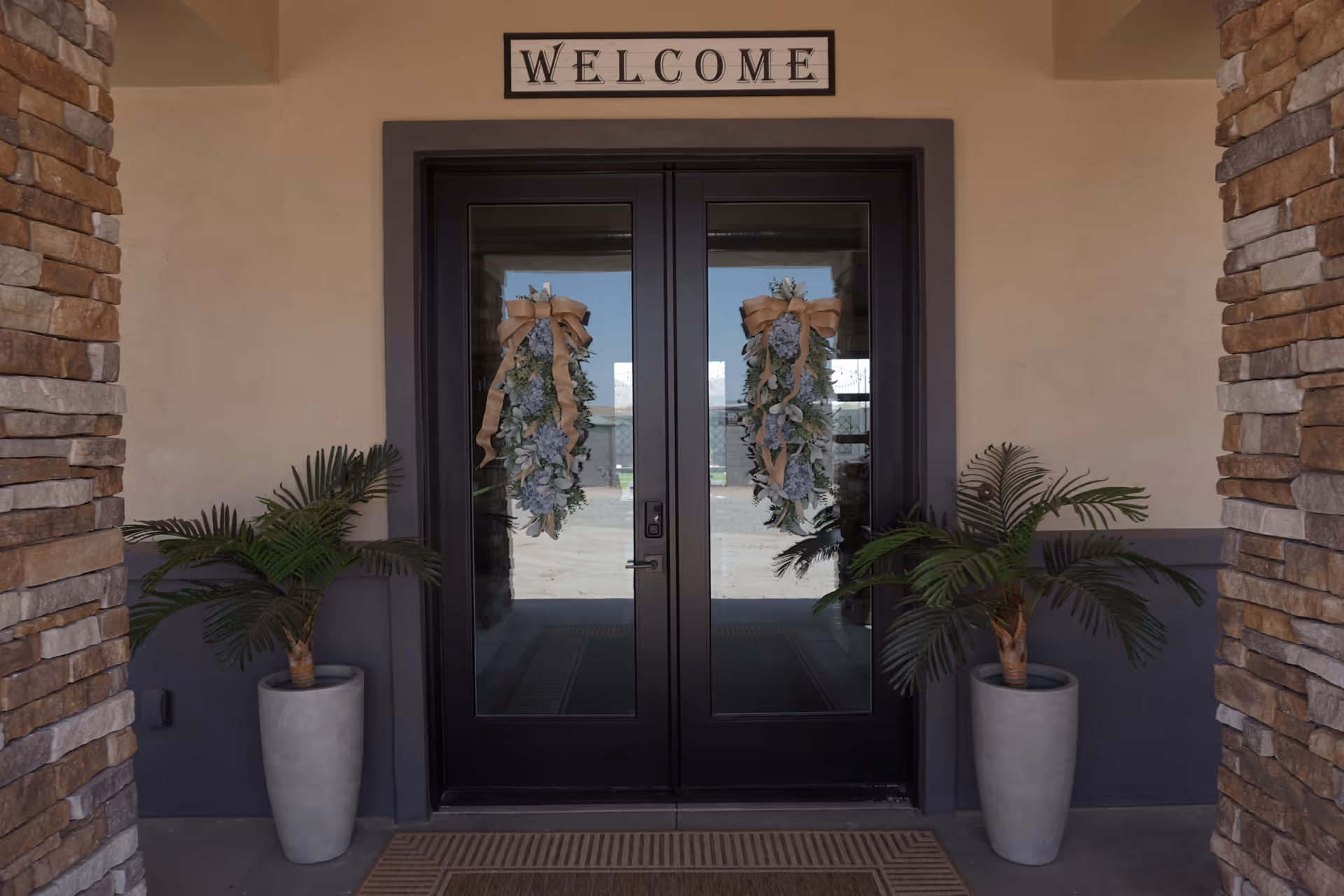 Sunset Villas entrance with double glass doors, welcome sign, and potted plants.