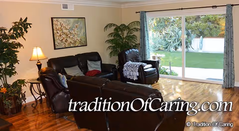 Cozy living room with black leather couches, plants, and a sliding glass door to outdoors.