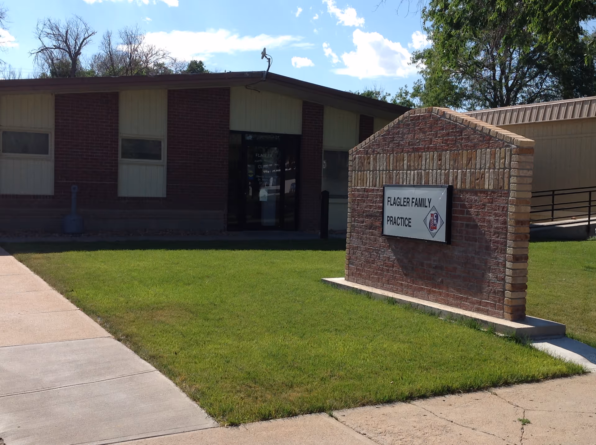 A brick clinic building exterior with a sign near the entrance.