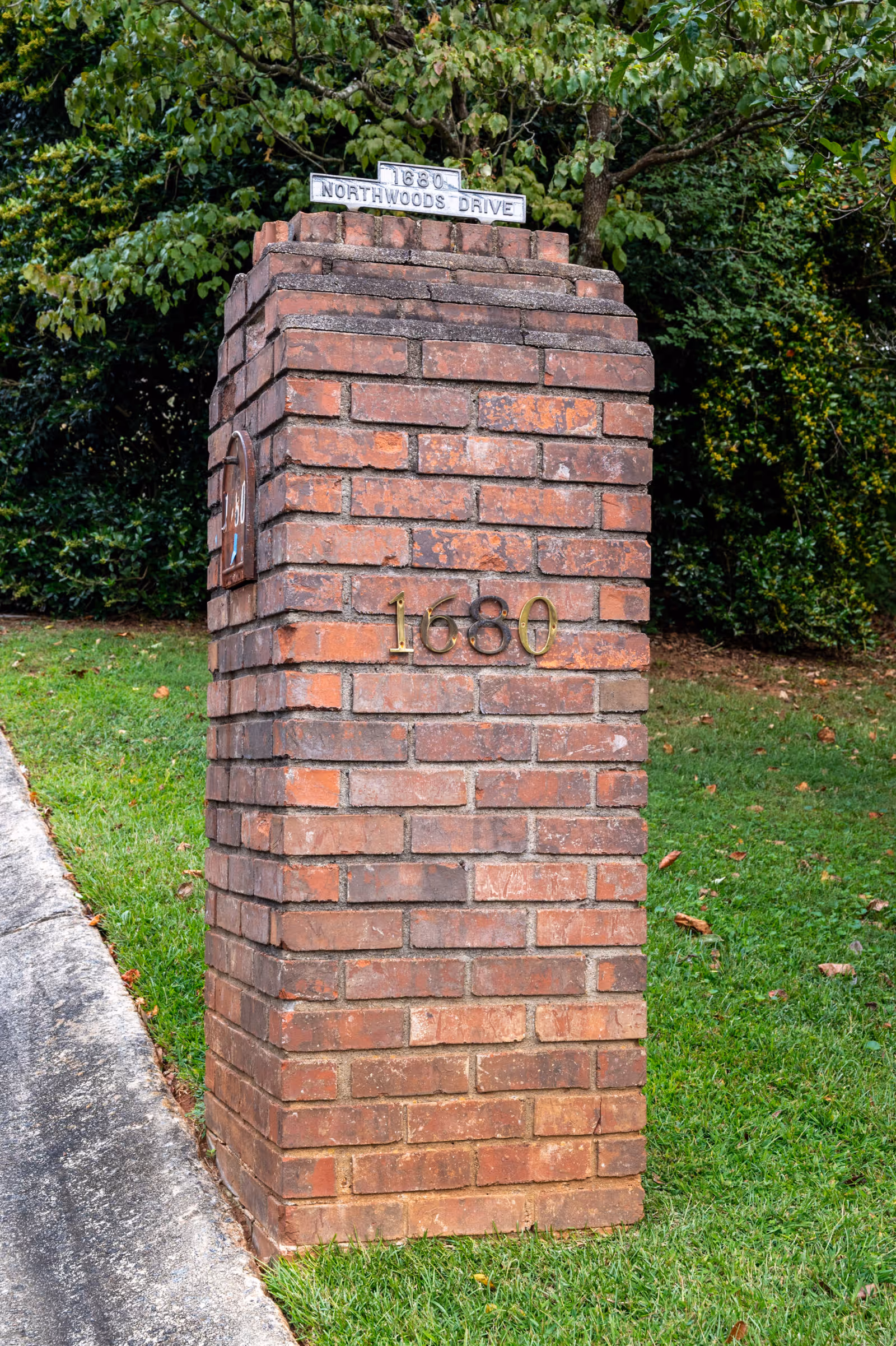 Brick pillar with address 1680 and Northwoods Drive sign beside green landscaping.