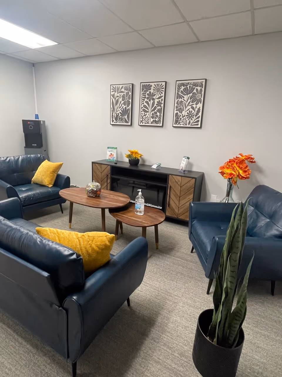 A contemporary senior-living lounge with blue leather sofas, round wood tables, and wall art.