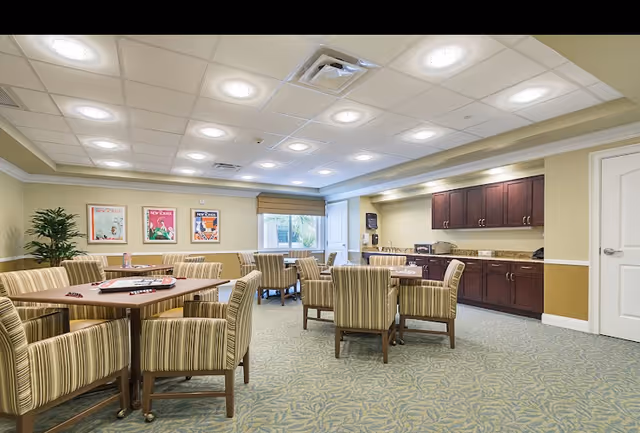 Common dining area with tables, striped chairs, and a kitchenette along the wall.