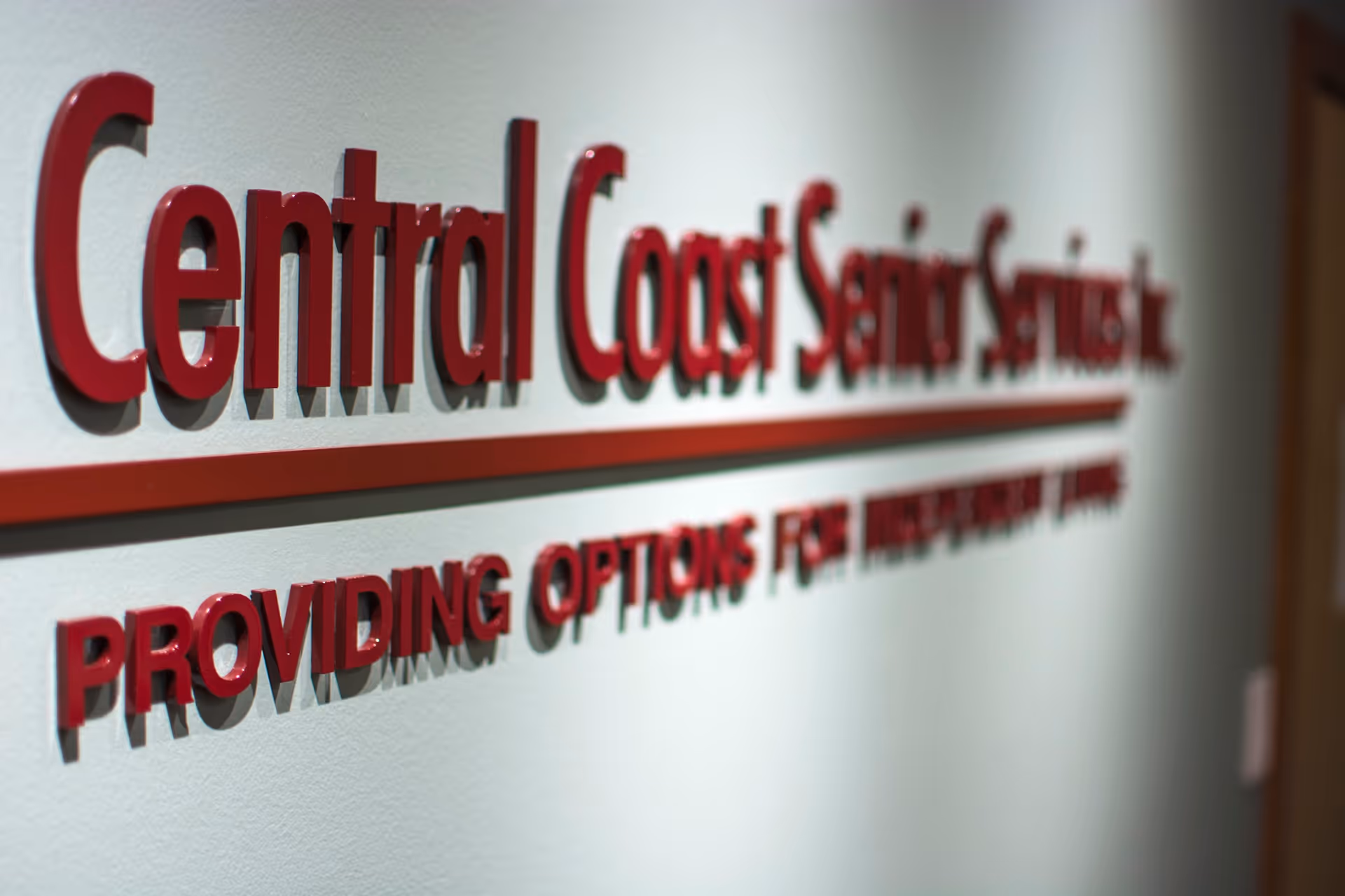 Red 3D sign reads Central Coast Senior Services, Inc., with a red underline on the wall.