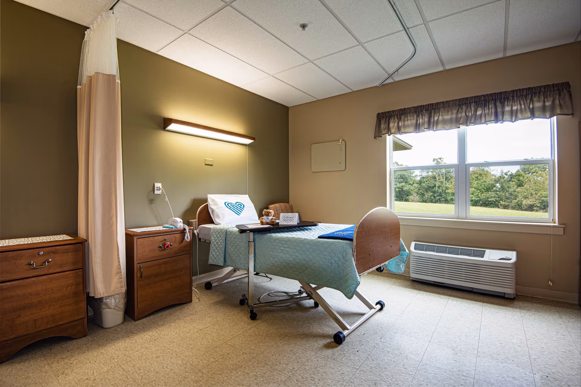 Hospital-style patient room with a bed, privacy curtain, nightstands, and a window.