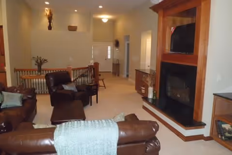 Senior living common room with brown leather sofas, a fireplace, and mounted TV.
