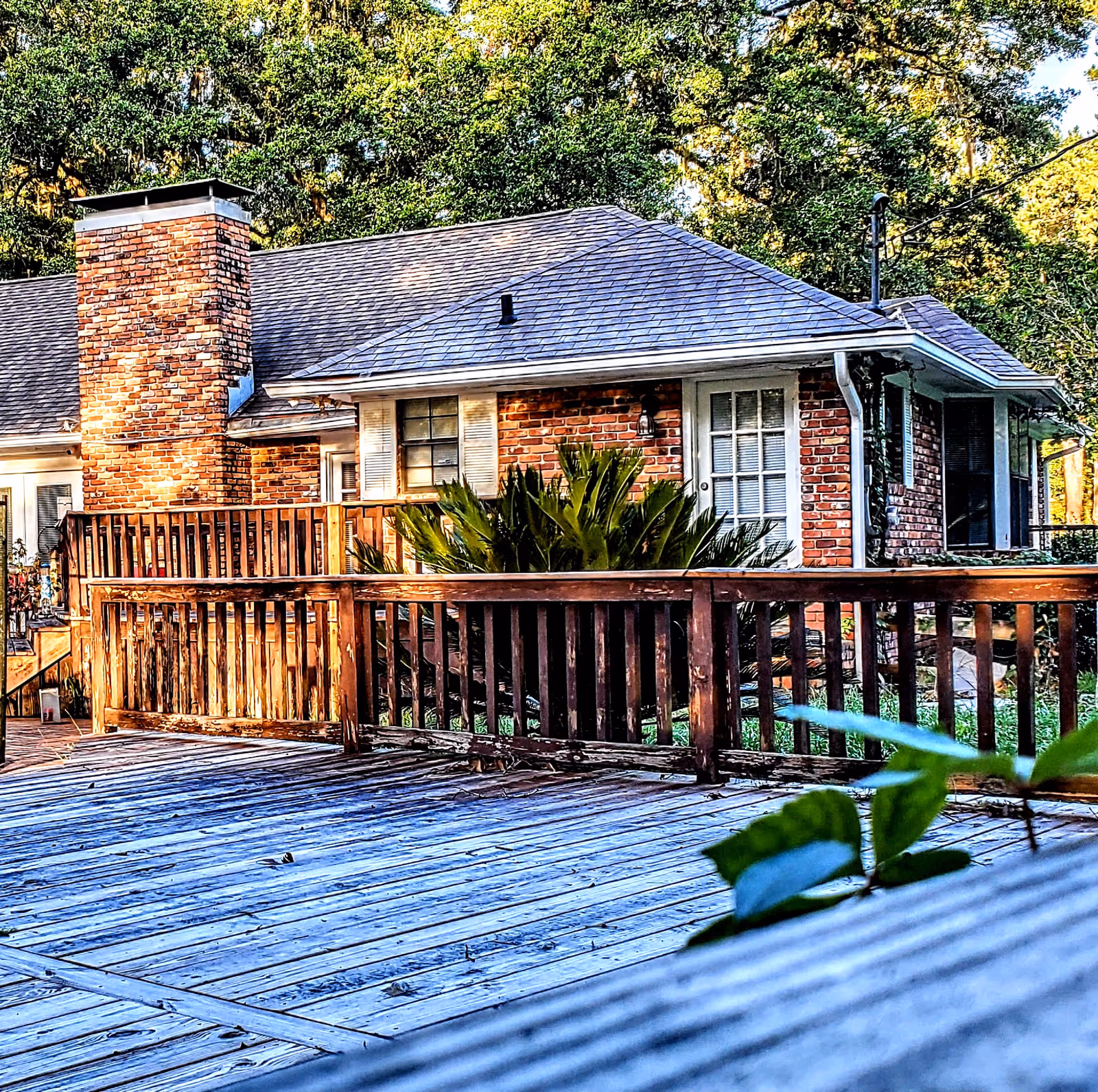 Brick, single-story residential home care with wooden deck railing and greenery.