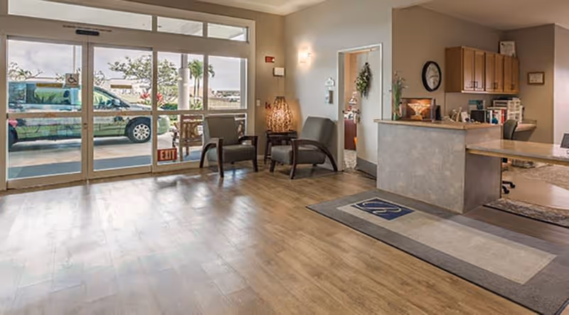 Spacious reception lobby with seating, a front desk, and glass entrance doors showing a vehicle outside.