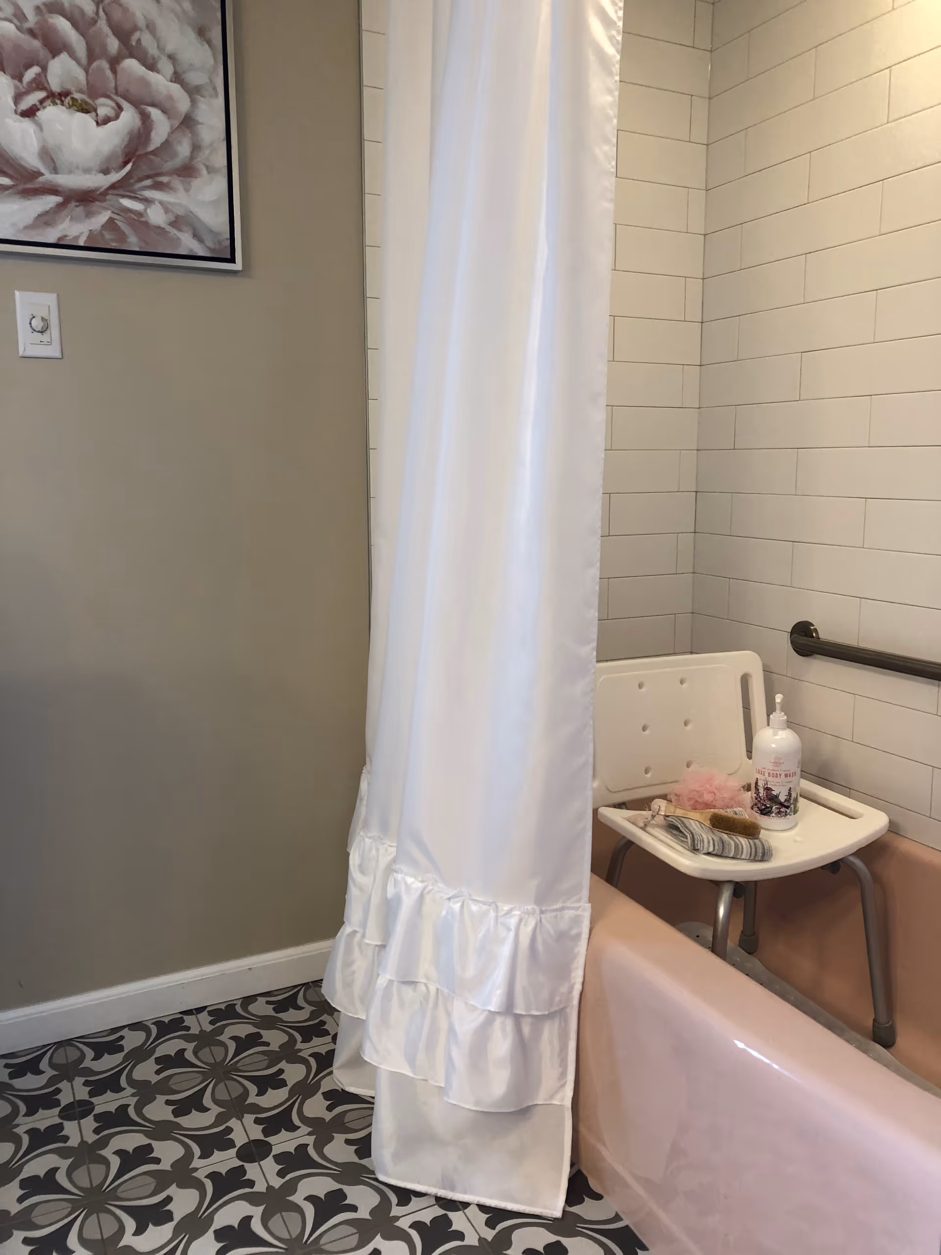 Pink bathtub with shower curtain, grab bar, and shower chair in tiled bathroom.