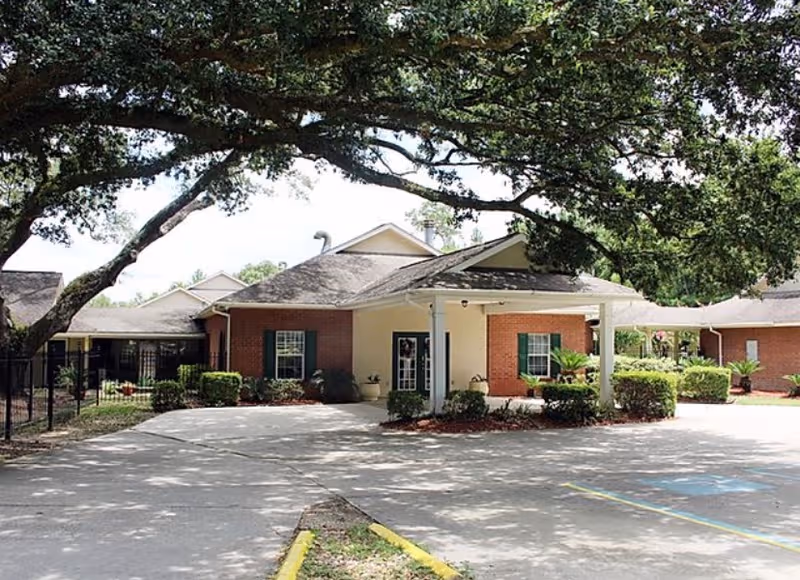 Single-story senior living facility with brick exterior, covered entrance, and a large tree overhead.