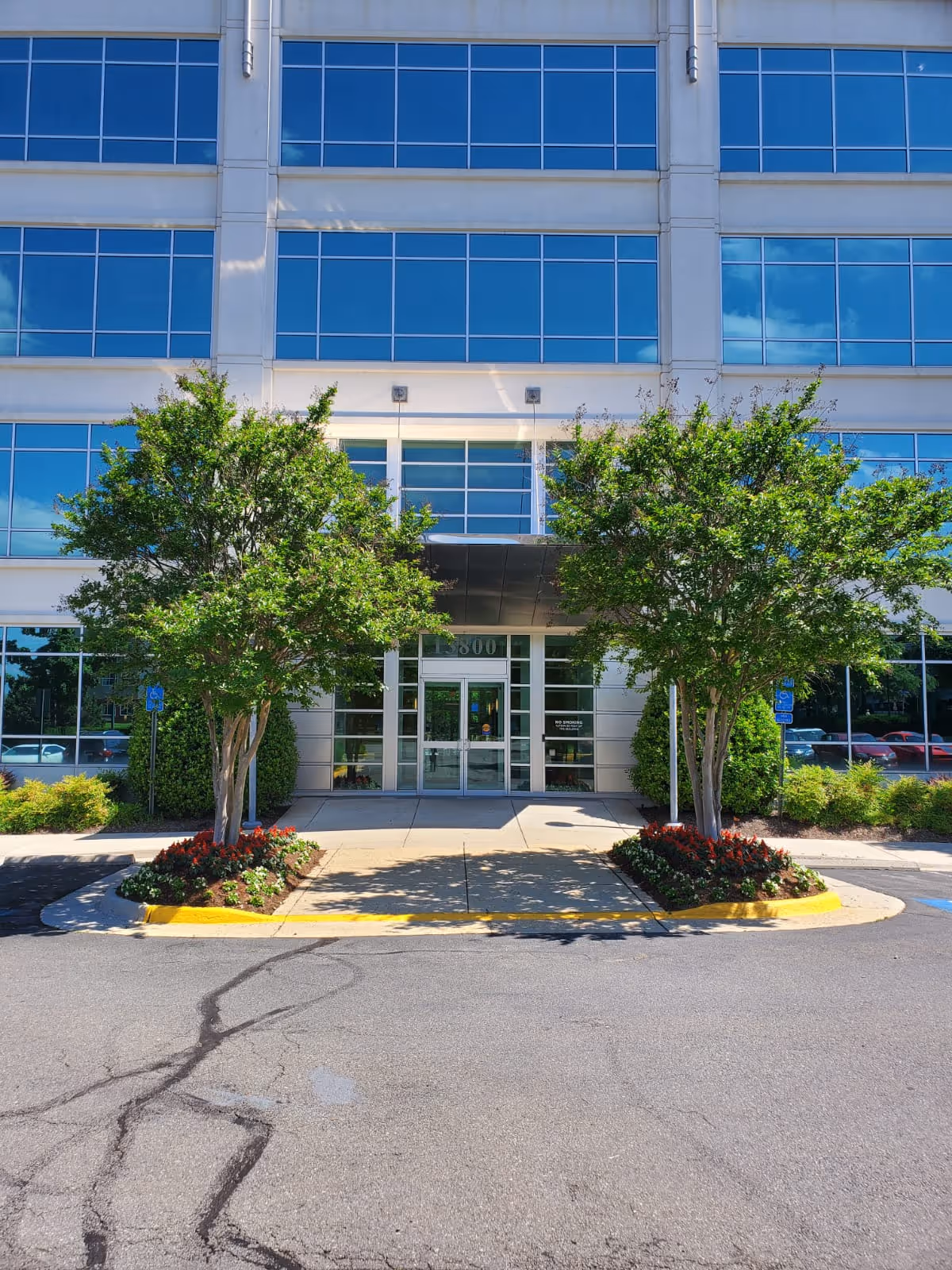 Modern glass-front senior living facility entrance framed by trees and planters.