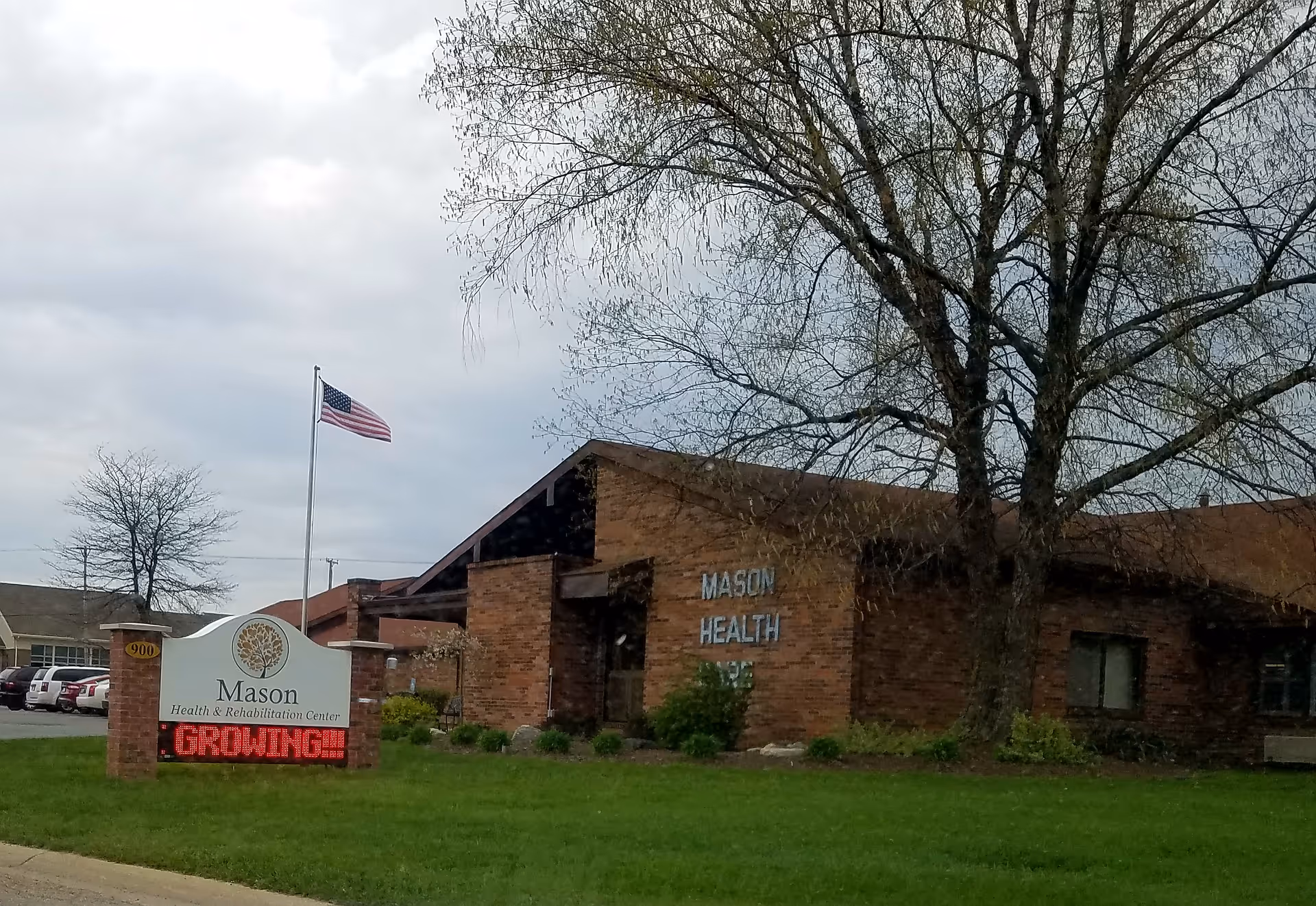 Brick Mason Health building with sign, American flag, and large trees in front lawn.