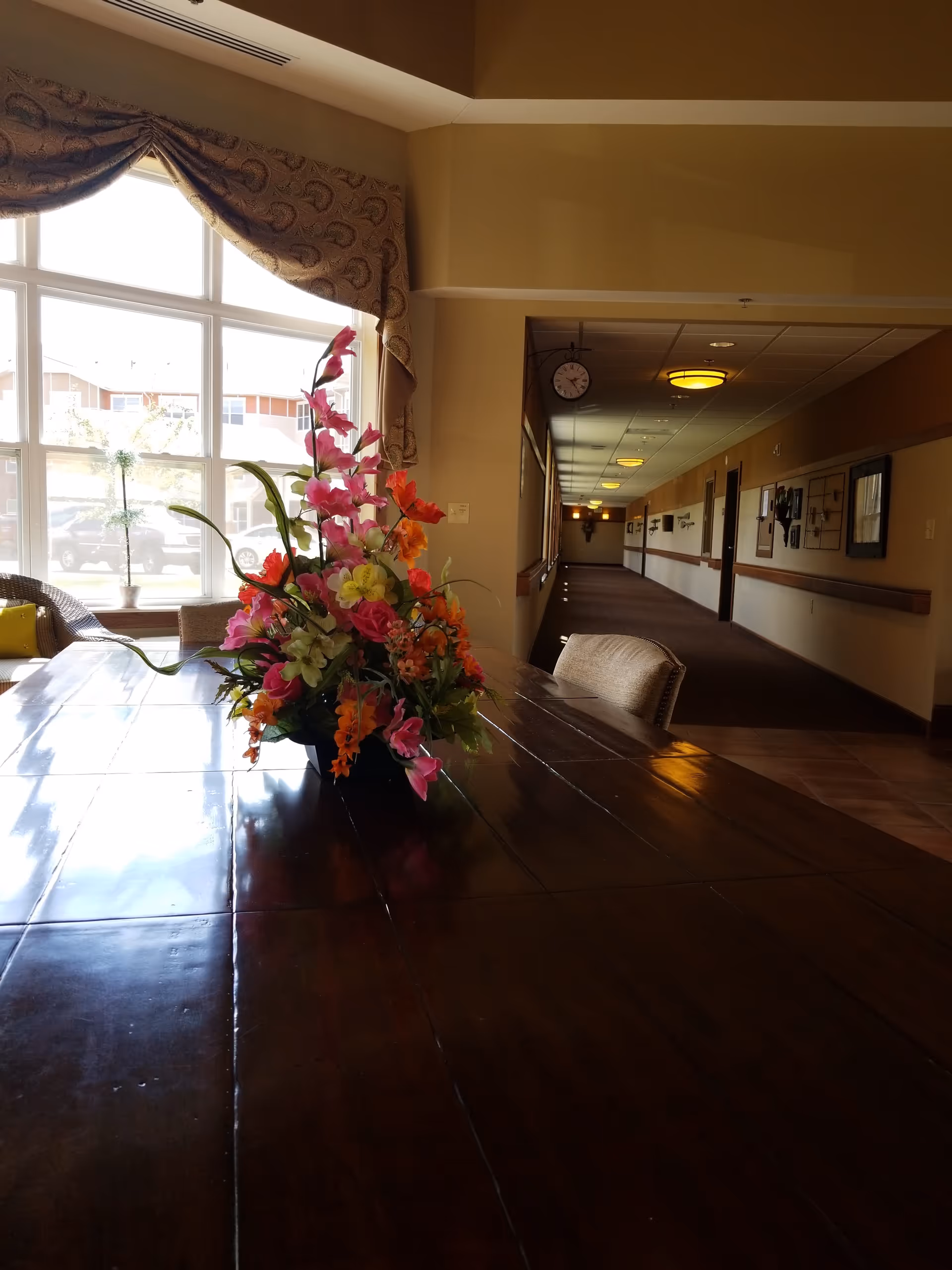 A long hallway inside a senior living facility with a flower arrangement on a table.