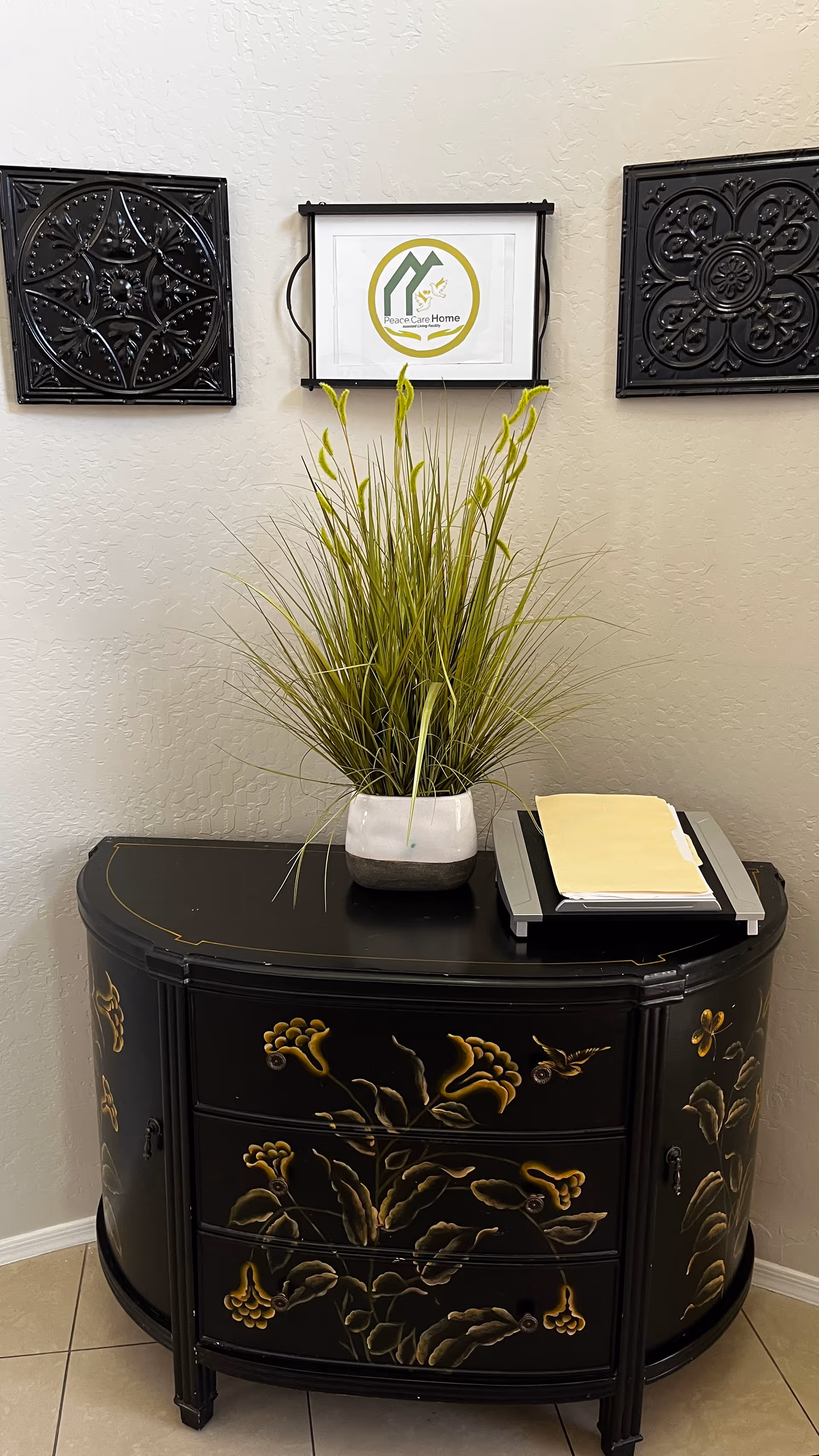 Indoor hallway with a black curved cabinet, tall plant, and a Peace Care Home sign.
