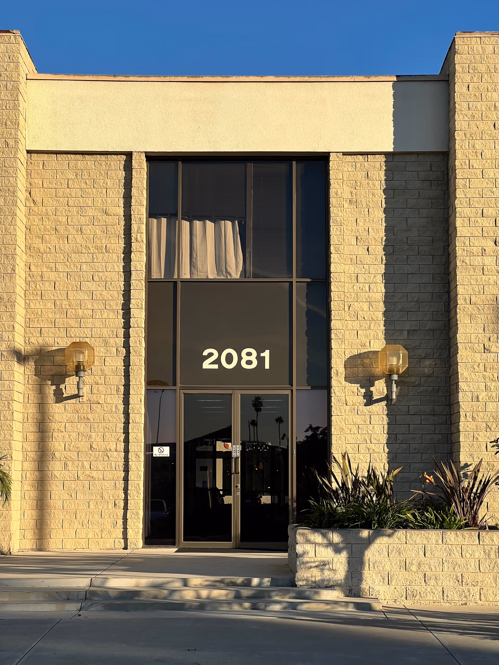 Front view of a beige brick building entrance with glass doors and the number 2081