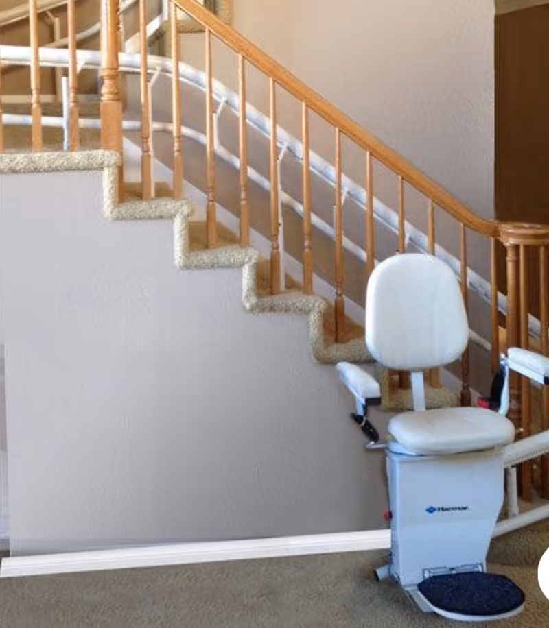 Indoor stair lift device installed along a carpeted staircase with wooden railing.