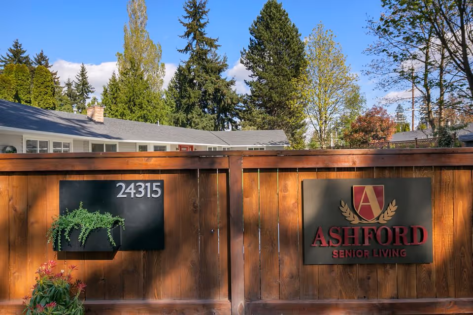 Wooden fence, Ashford Senior Living sign, address 24315, with a building and trees behind