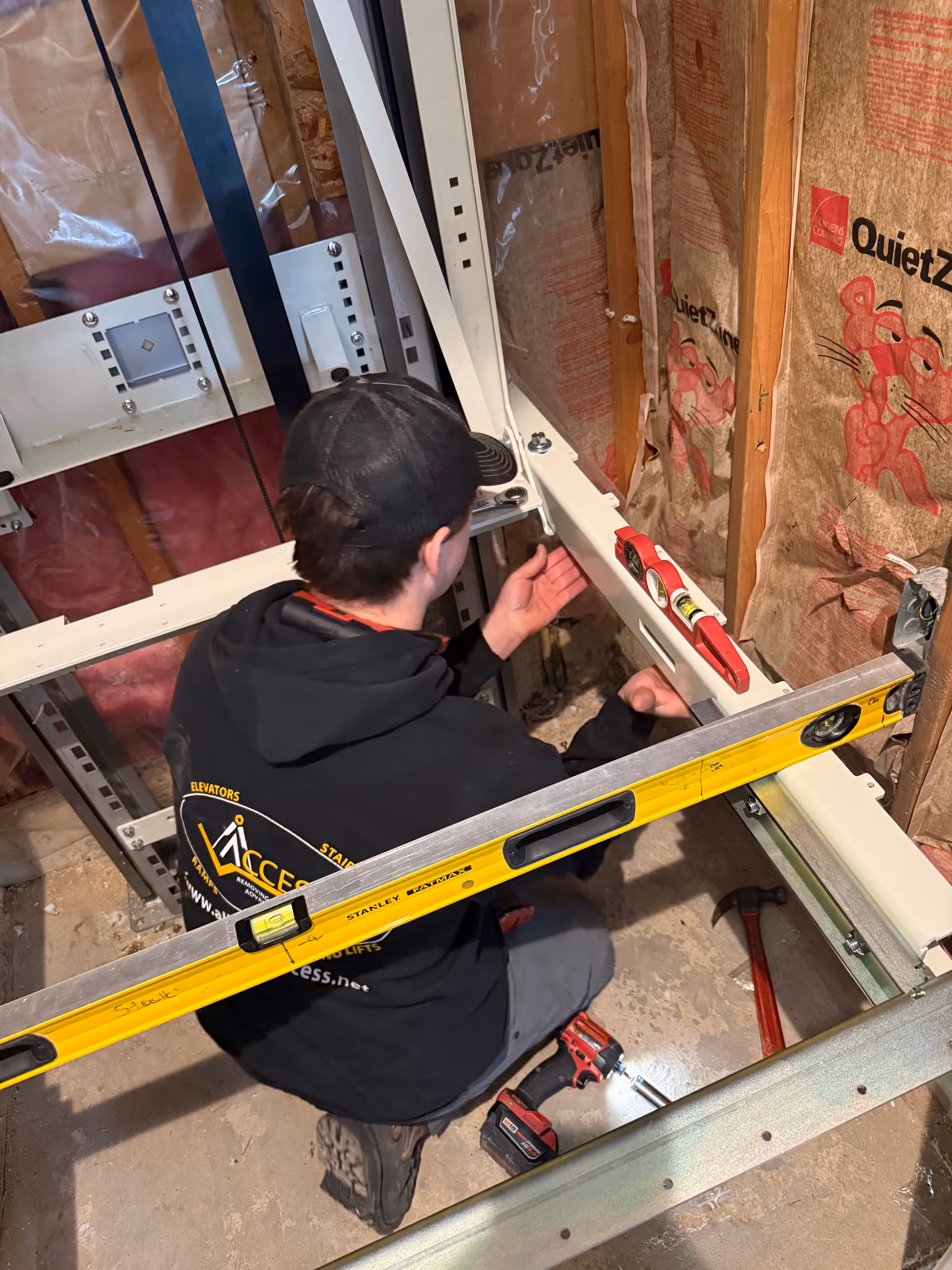 Construction worker installing elevator components inside a partly unfinished interior with exposed insulation.