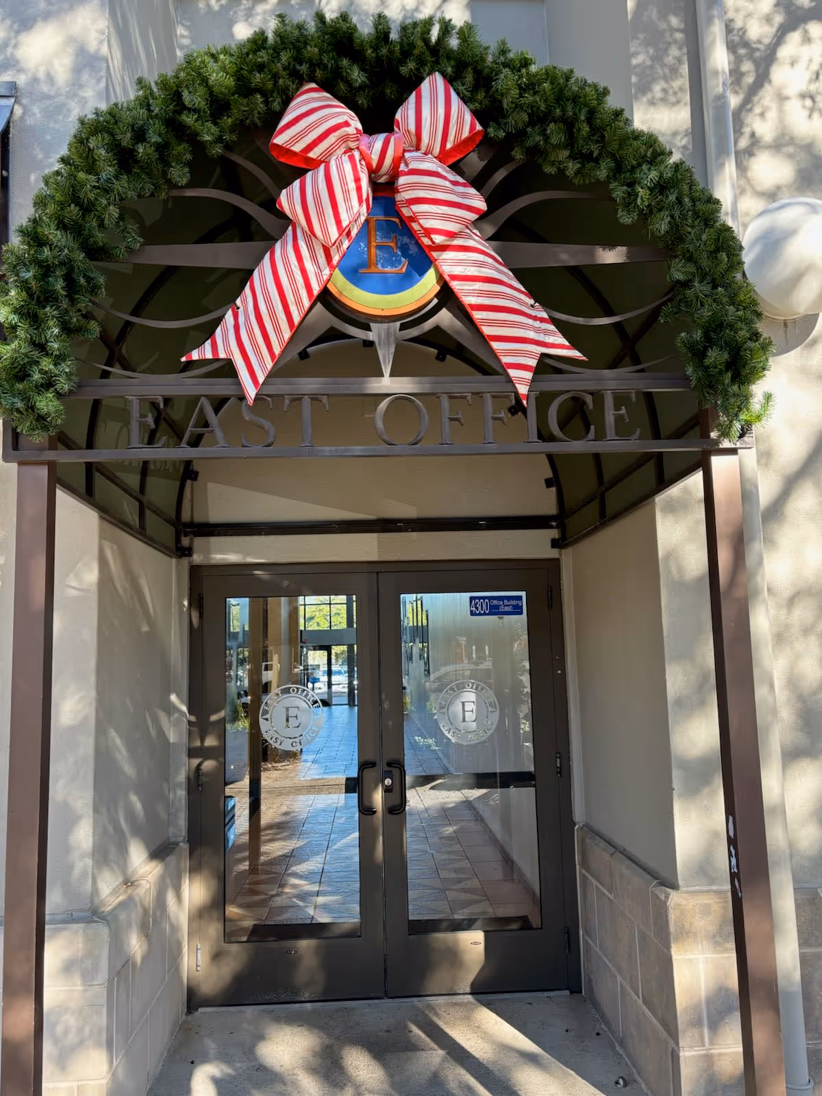 Exterior entrance to senior home care building with green wreath and red ribbon above glass doors.