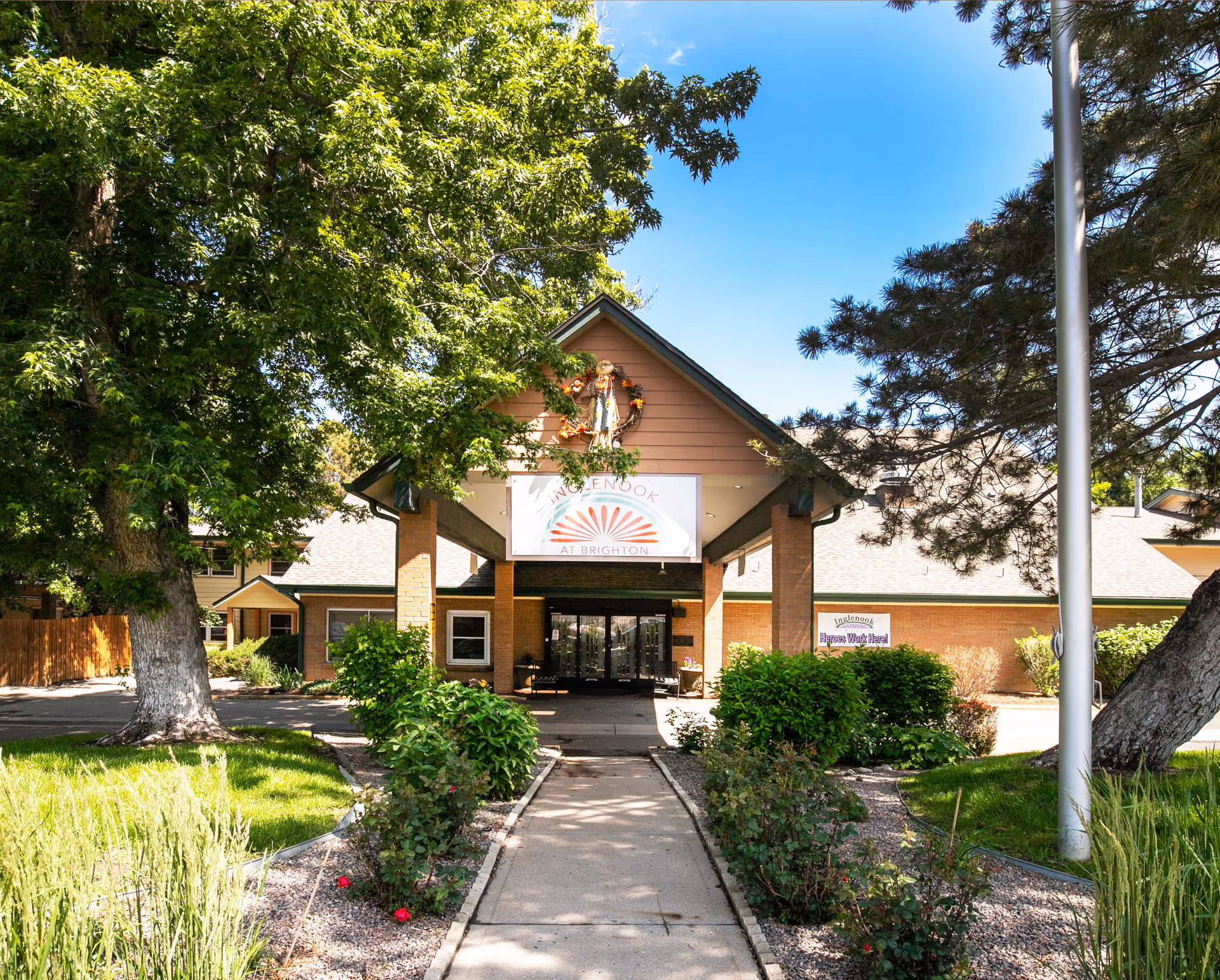 Entrance to Inglenook at Brighton senior living facility with trees, walkway, and signage.