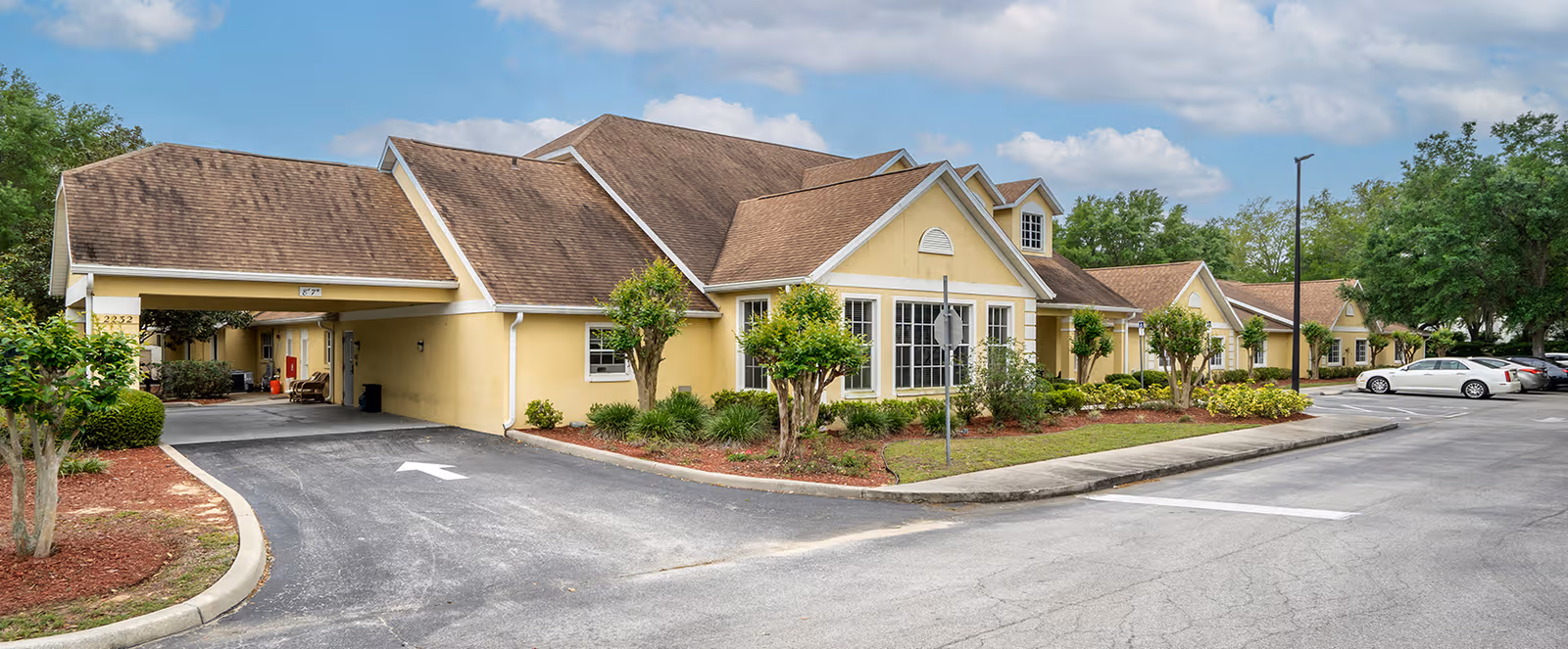 Wide exterior view of Brookdale Tavares campus with yellow buildings, driveways, and parked cars.