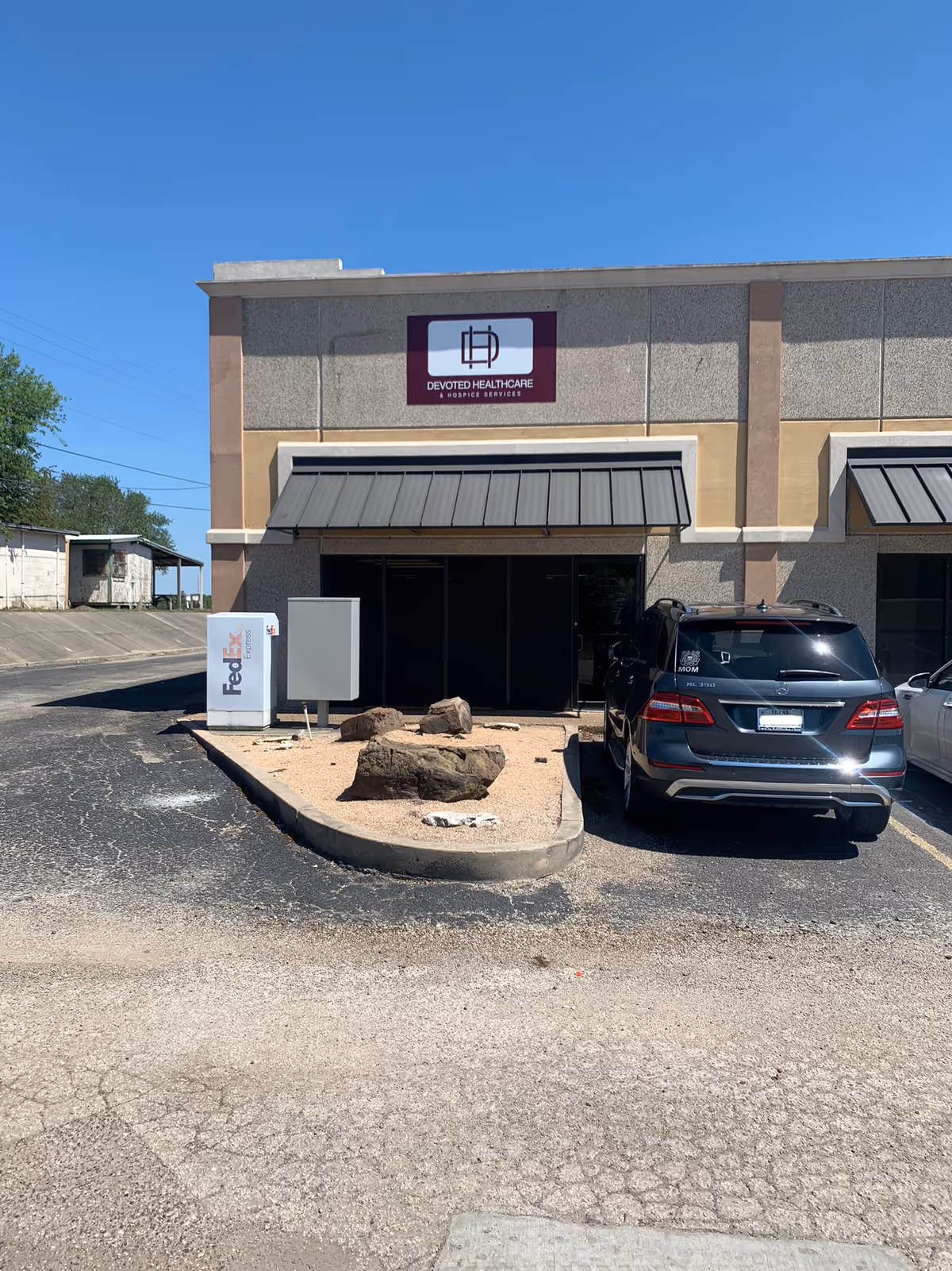 Exterior view of Devoted Healthcare building with front entrance, car, and FedEx drop box.