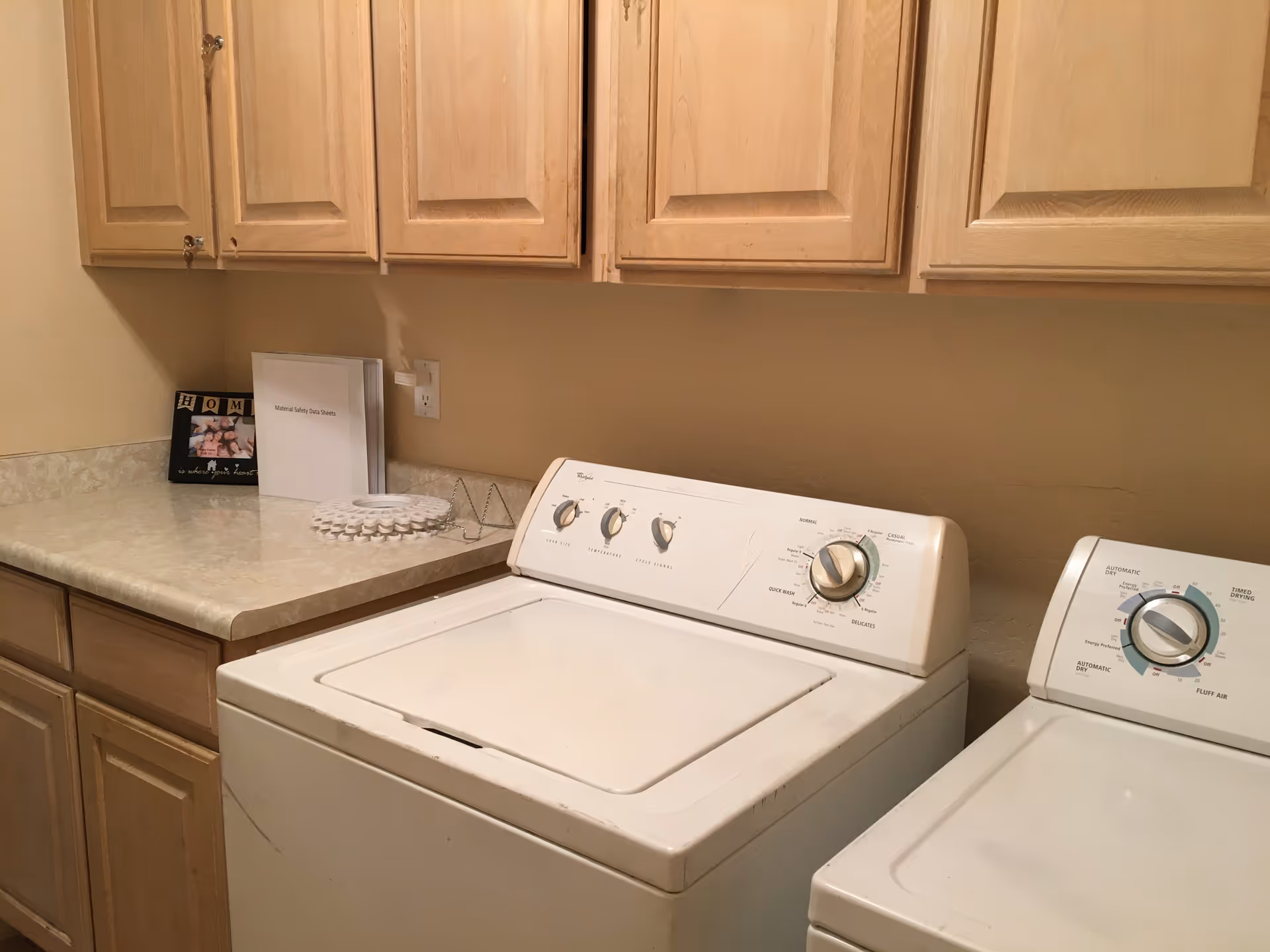 Laundry room with a washer, dryer, and wooden cabinets along beige walls.